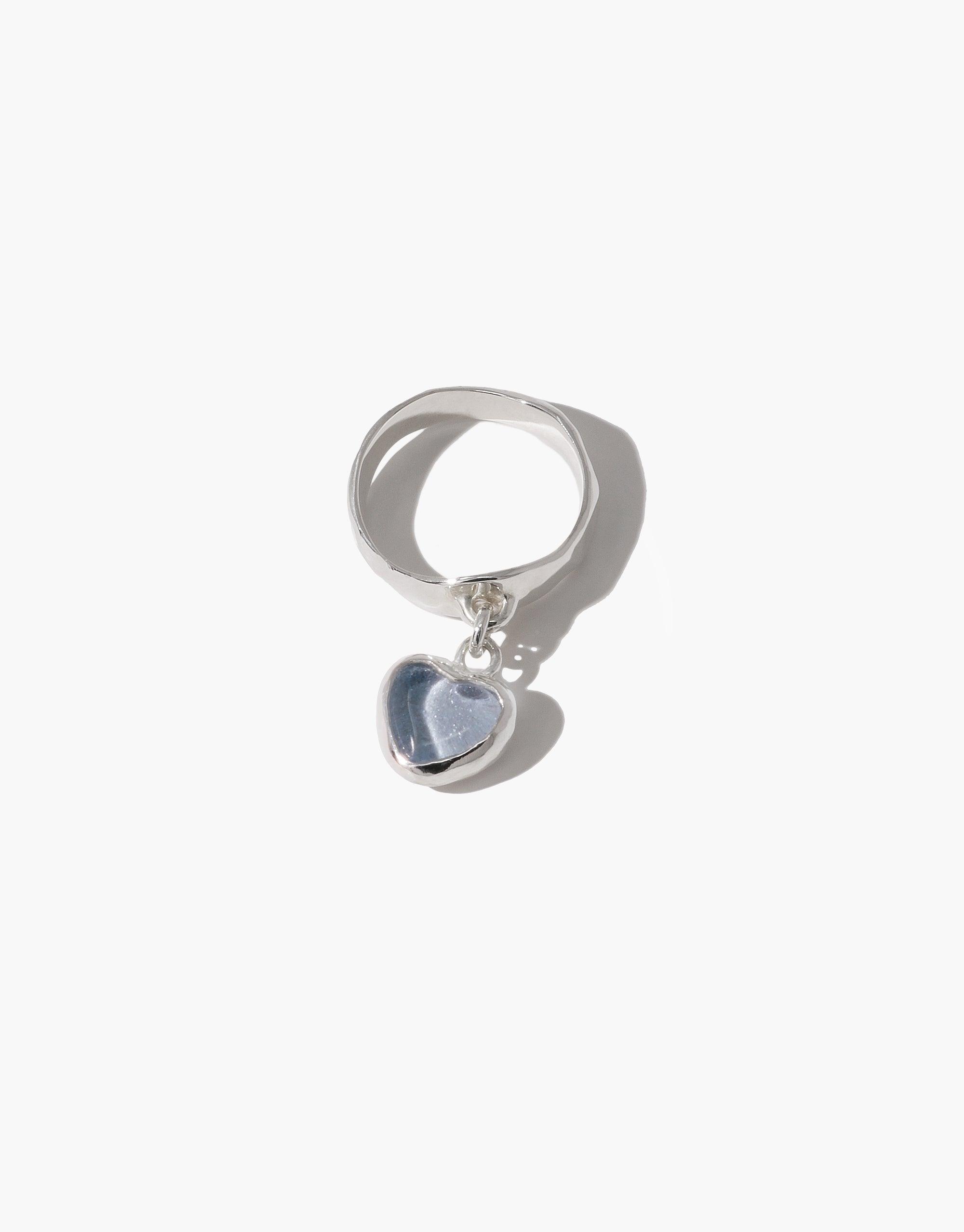 Heart Dangling Ring featuring a silver band with a small heart-shaped charm in light blue, suspended from the ring. Handcrafted design showcasing upcycled eco gem repurposed from glass bottles. Elegant and environmentally conscious jewelry piece by CLED.