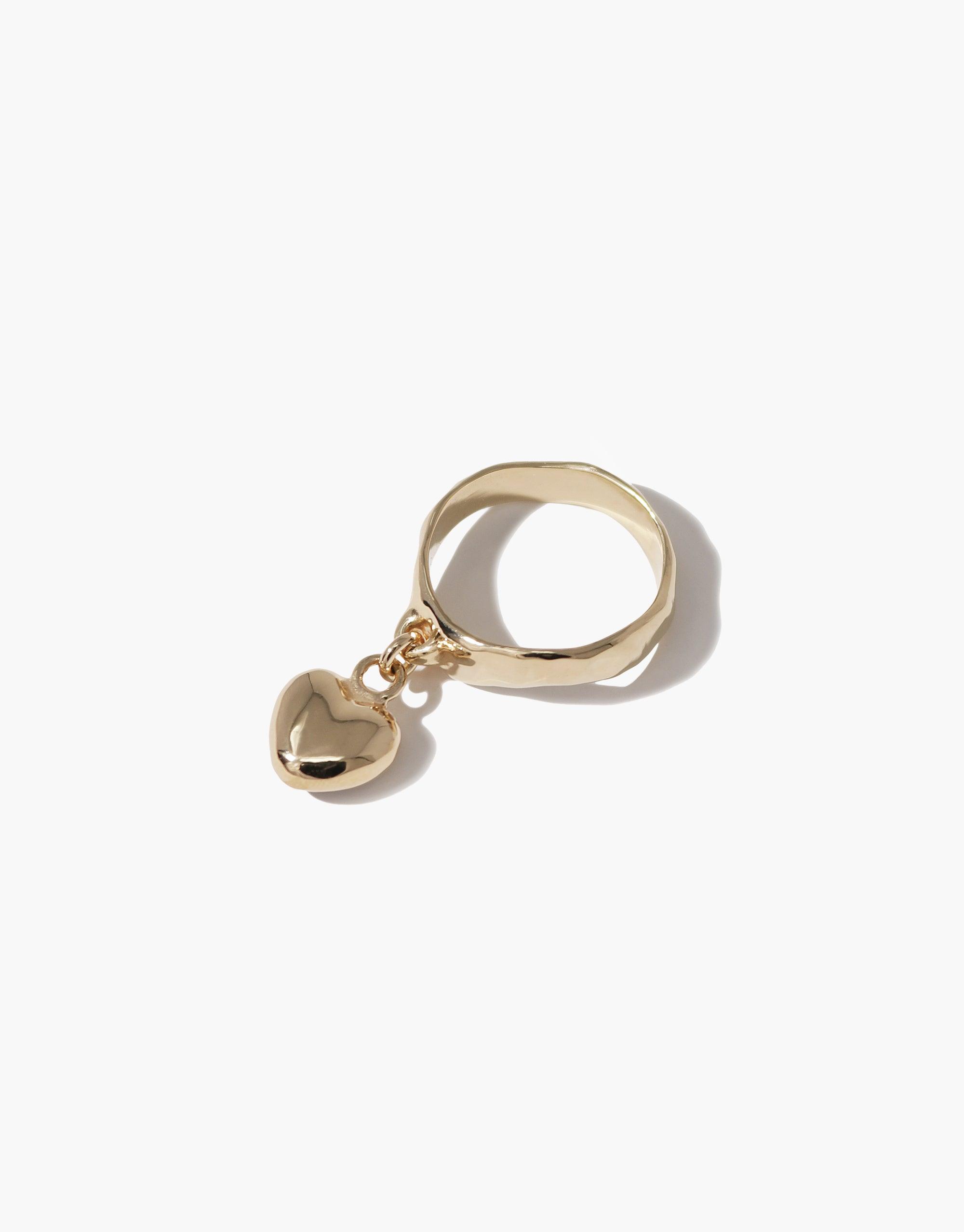 Heart Dangling Ring featuring a gold-toned band with a small heart-shaped charm hanging from it. The ring showcases a minimalist design with a polished finish, perfect for everyday wear or as a statement piece. Handcrafted with eco-friendly materials. CLED