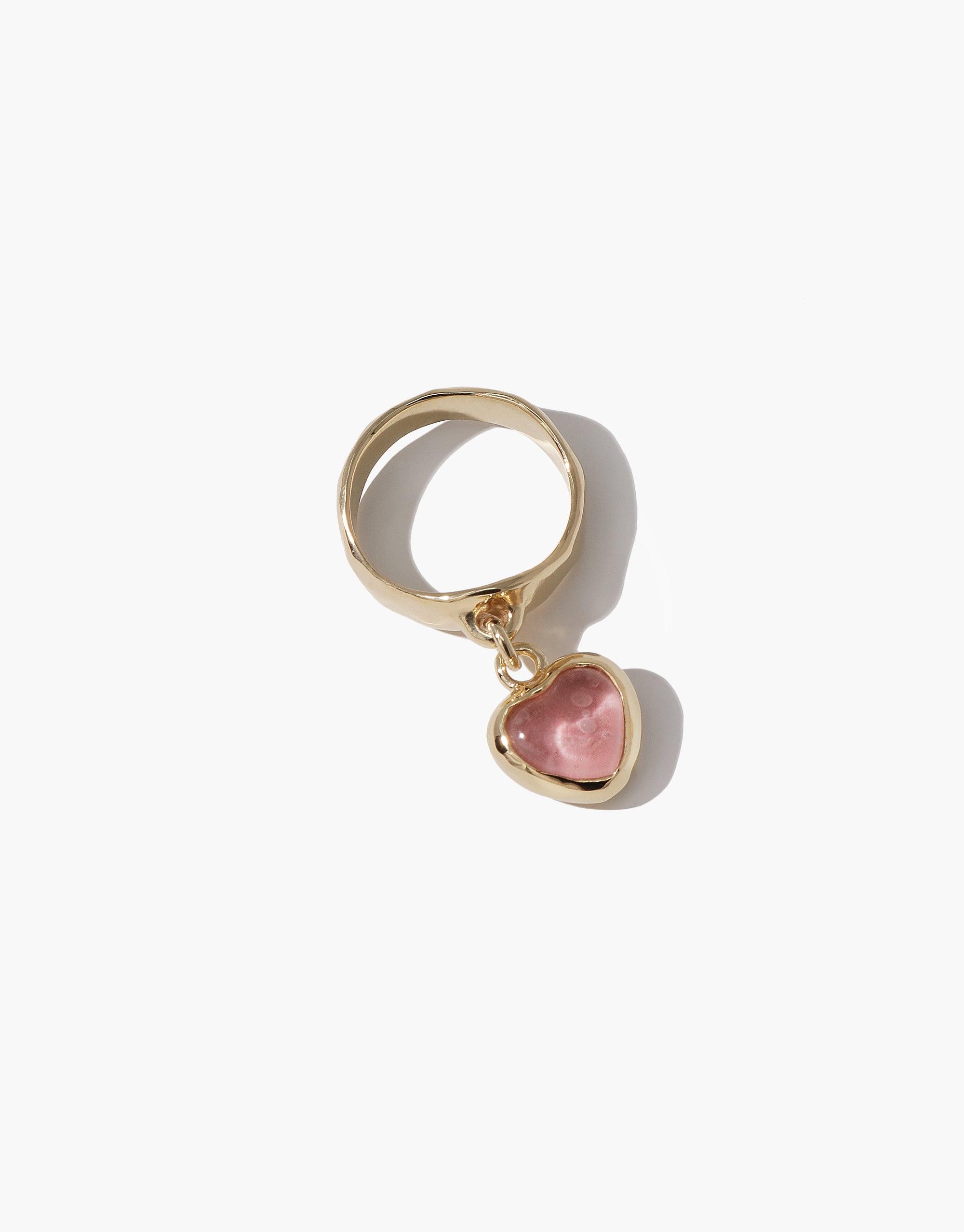 Gold-toned ring with a dangling pink heart-shaped charm, showcasing the Heart Dangling Ring. Handcrafted design featuring upcycled eco gem, perfect for sustainable jewelry enthusiasts. CLED