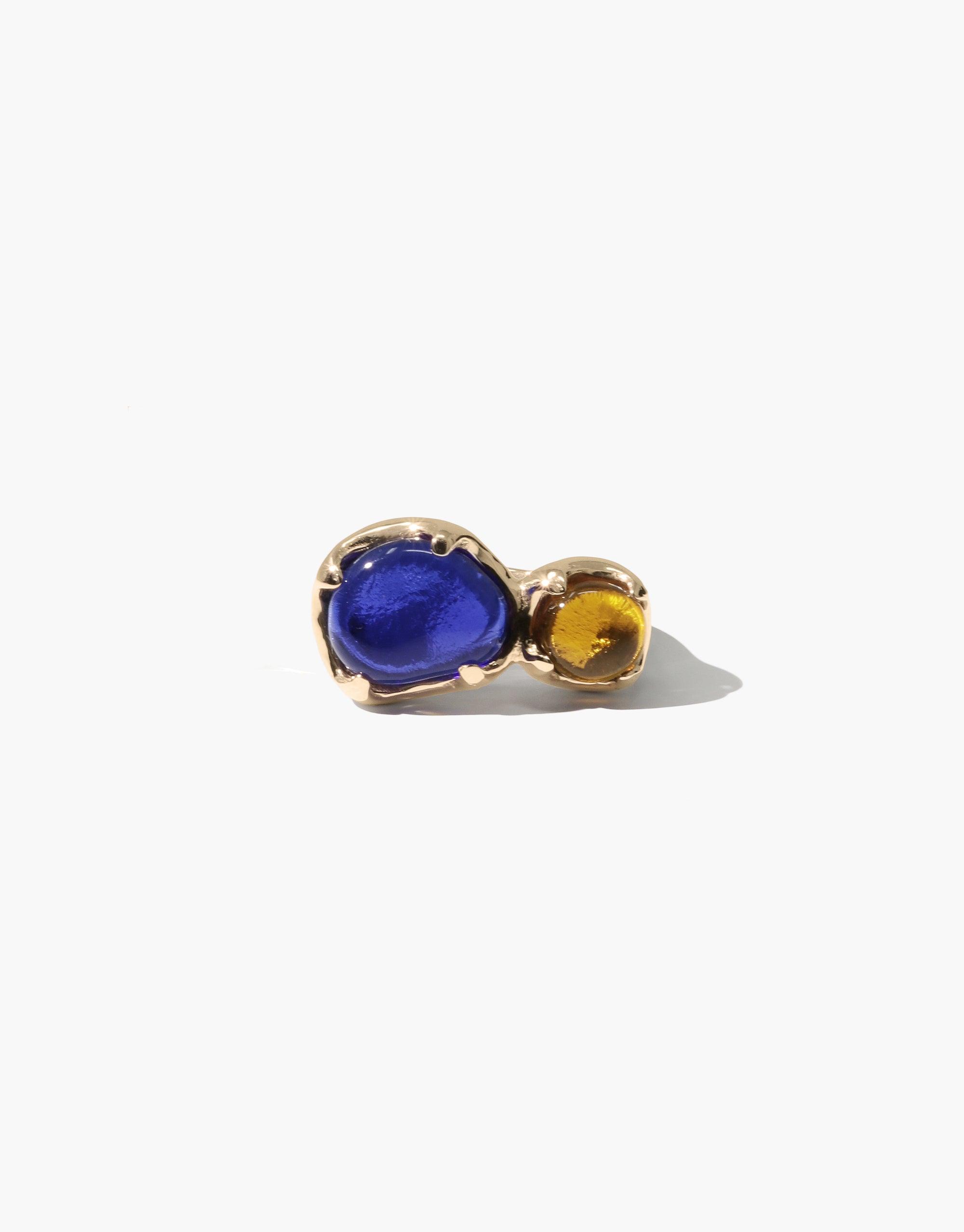 Duo Beam Ring featuring vibrant blue and amber eco gems set in gold-toned metal, showcasing unique color contrast and sustainable design. Handcrafted jewelry piece inspired by prismatic light refraction. CLED