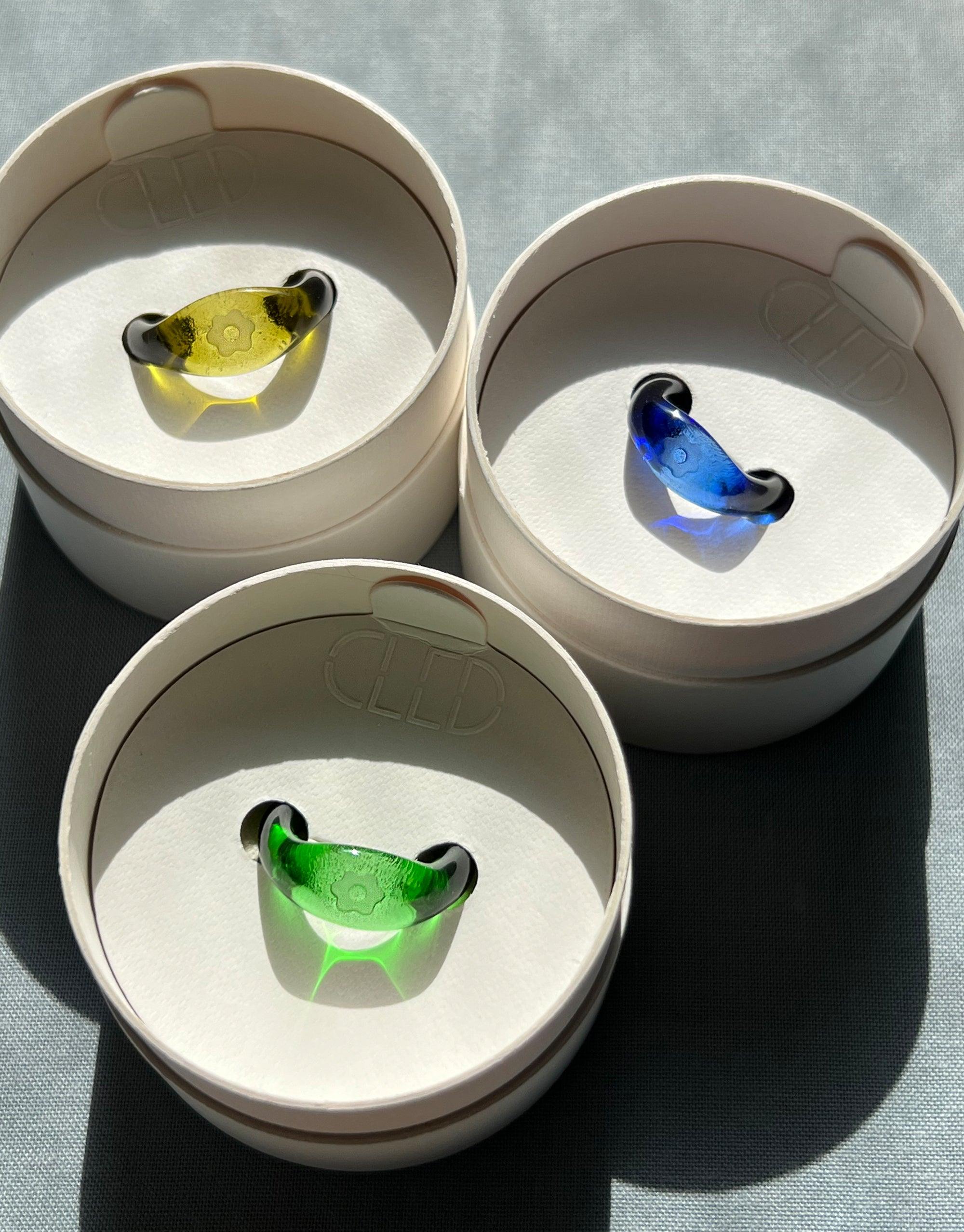 Avens Signet Rings in yellow, blue, and green eco gems displayed in white circular boxes, showcasing the unique handcrafted design of the Messenger Collection by CLED