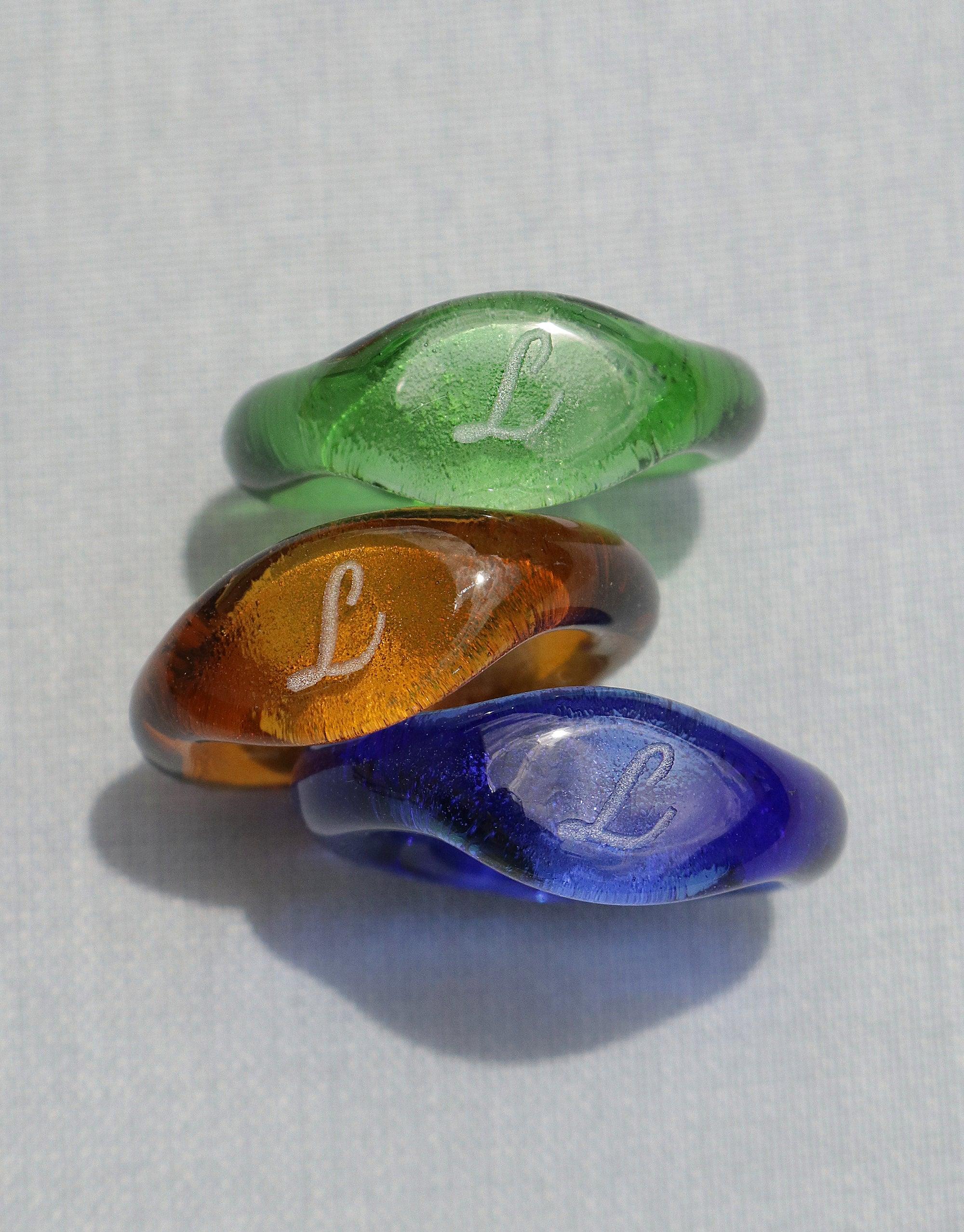 Engravable Signet Ring in vibrant eco-friendly glass colors - green, amber, and blue. Each ring features a personalized 'L' etching, showcasing the unique handcrafted design of the Messenger Collection. Sustainable, customizable jewelry by CLED.