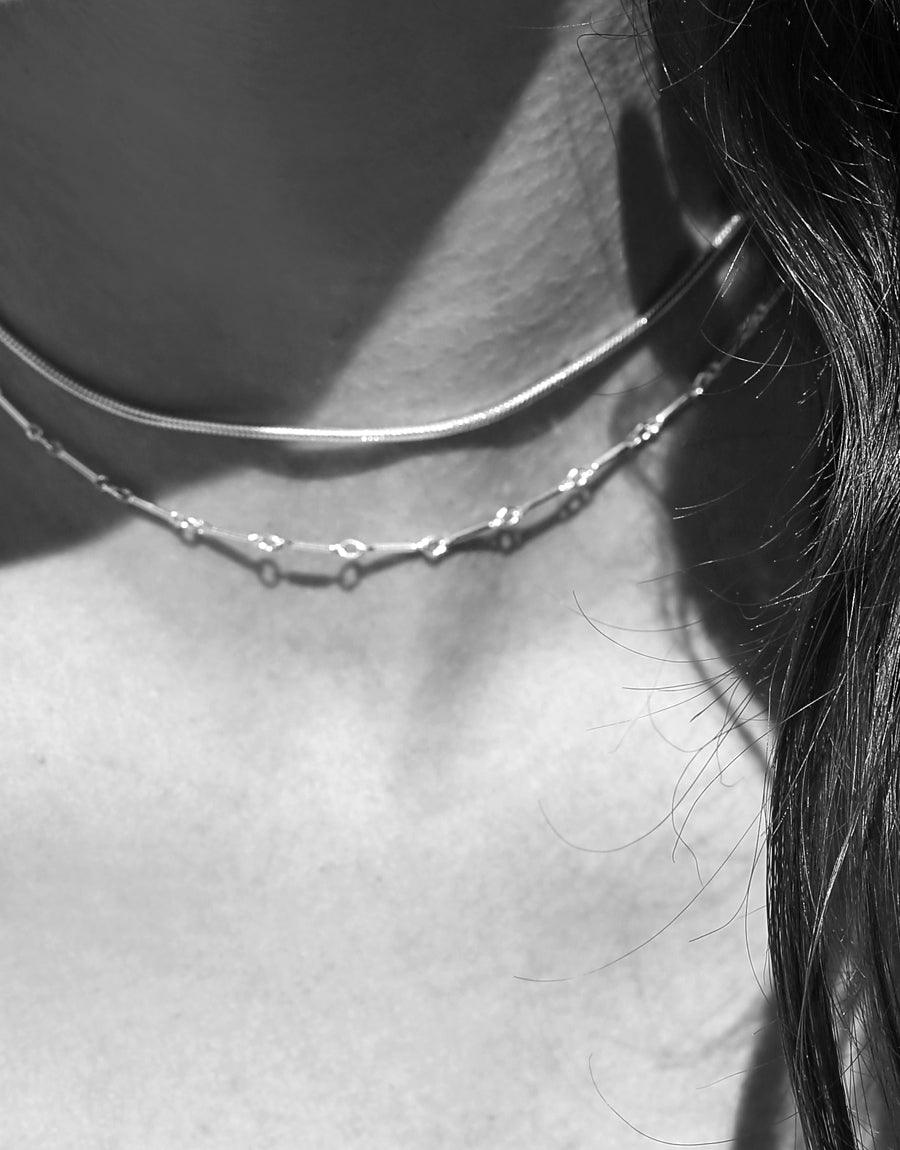 Close-up black and white image of a neck wearing a delicate Linked Bar Choker Necklace. The sterling silver chain features small linked bars, showcasing its elegant design. Perfect for everyday wear and layering. Handcrafted in Los Angeles by CLED.