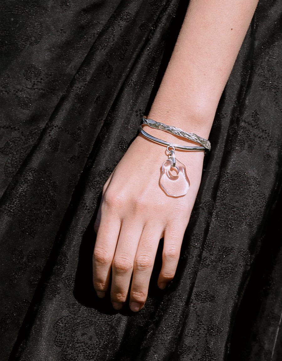 Elegant Coastline Drop Bracelet featuring sterling silver bands and eco-friendly glass pendant, worn on a wrist against a dark background. Handcrafted cuff design inspired by seashore curves. Sustainable jewelry by CLED.