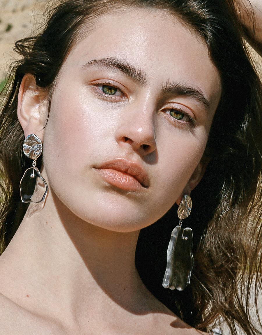 Elegant model wearing Coastline Earrings Small Drop, featuring recycled glass eco gems and sterling silver. Handcrafted design inspired by coastal shapes, showcasing sustainable luxury jewelry. Unique statement piece by CLED.