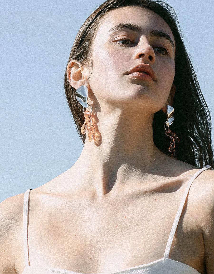 Wave Earrings: Close-up of a woman's neck showcasing wavy, organic-shaped earrings in sterling silver, reflecting an artful, nature-inspired style. Made in Los Angeles, these pieces are handcrafted to order.