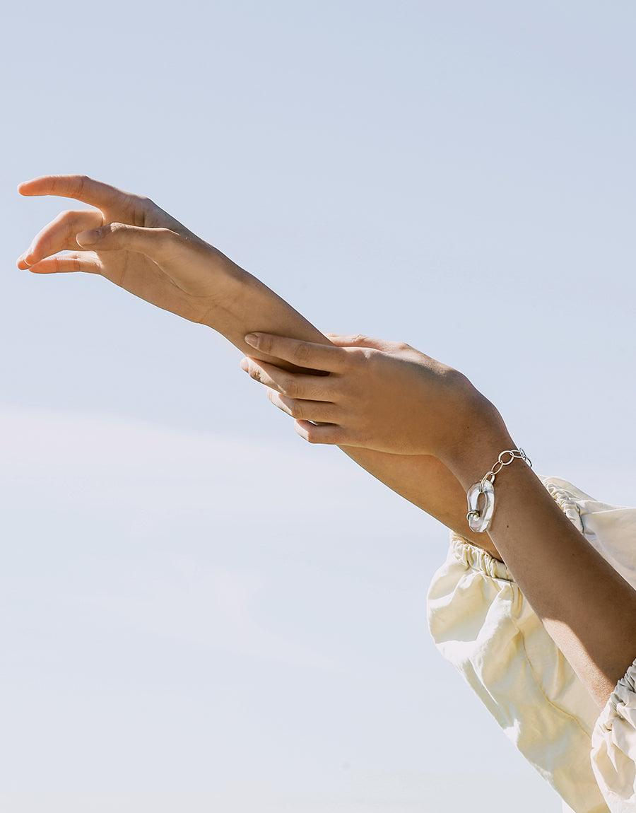 Elegant hands showcasing the High Tide Oval Chain Bracelet, a sterling silver statement piece with organic free shape and eco-friendly glass accent. Handcrafted in Los Angeles by CLED.