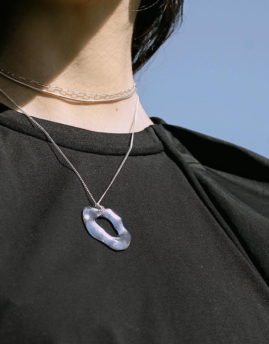 Close-up of a person wearing a delicate silver oval choker necklace paired with a longer necklace featuring an oval pendant. The necklaces contrast beautifully against a black top, showcasing layered styling. Oval Choker Necklace by CLED.