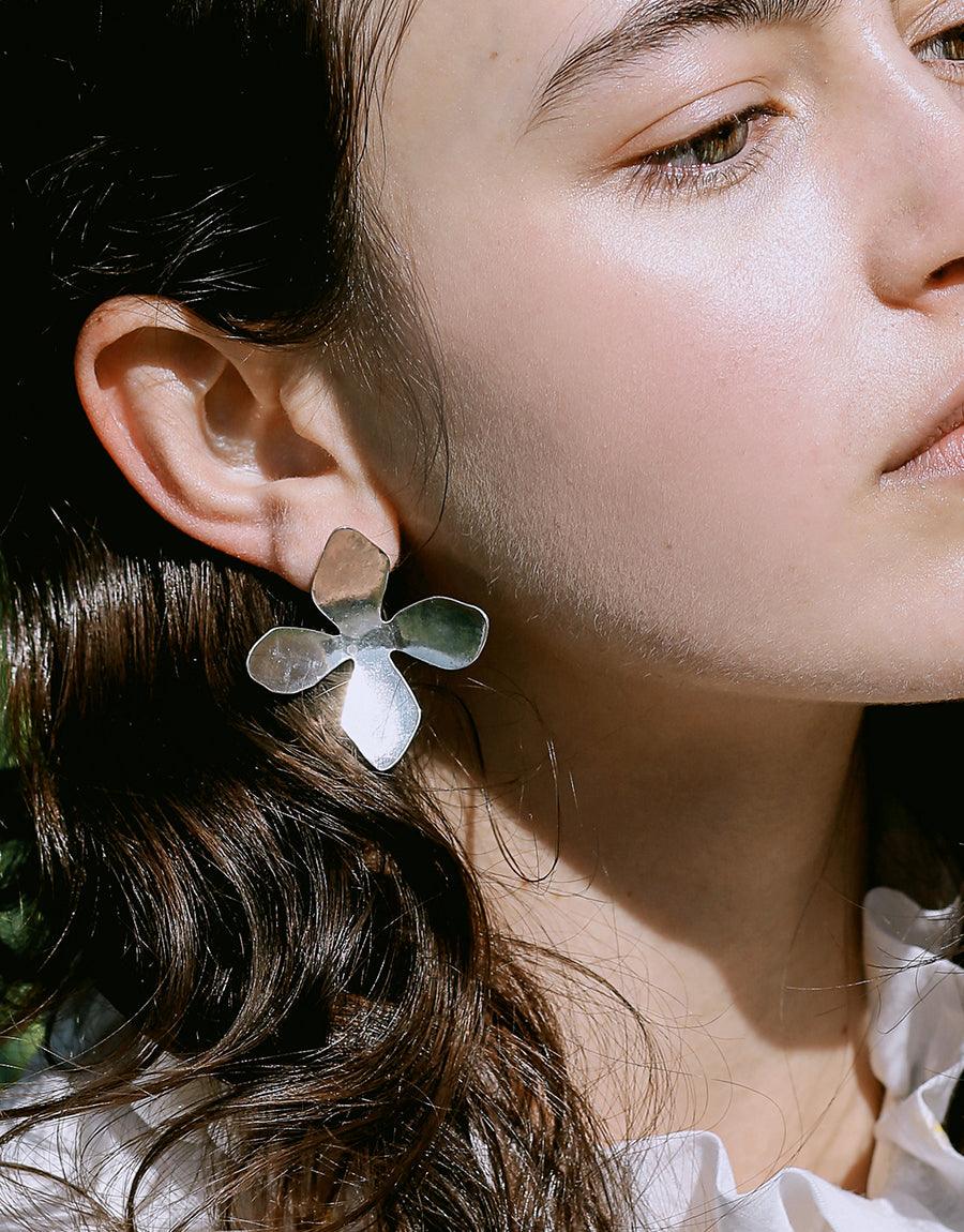 Close-up of Petal Earrings, featuring a delicate flower-shaped design in recycled sterling silver. The earring elegantly adorns the ear, showcasing its 1.5-inch length and handcrafted nature. Inspired by California wildflowers, this CLED Petal Earrings piece embodies springtime beauty.