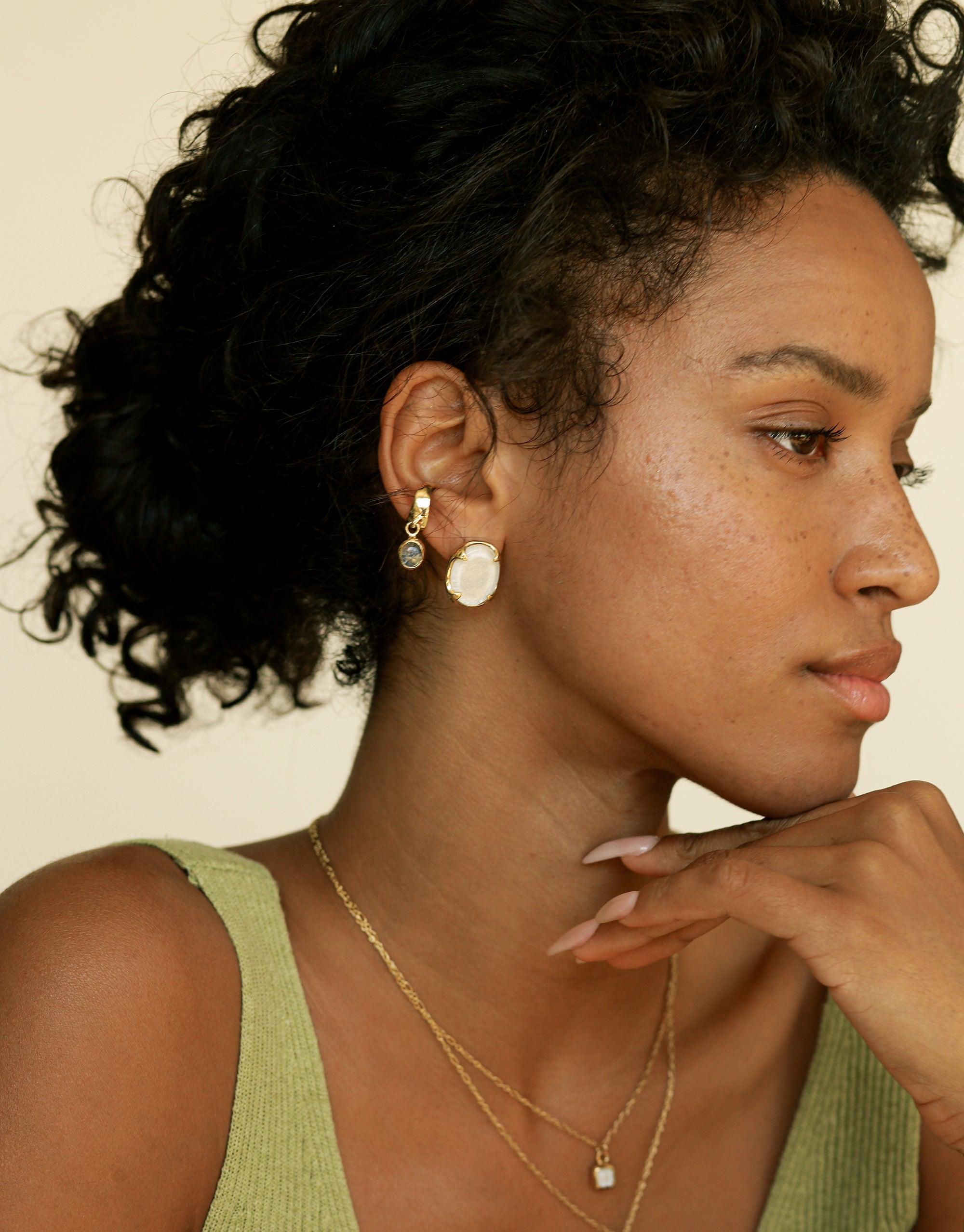 Side profile of a person wearing an oval dangling ear cuff with a unique charm, showcasing the elegant design and craftsmanship of the handmade jewelry piece. The Oval Dangling Ear Cuff by CLED adds a subtle yet stylish accent to the wearer's look.