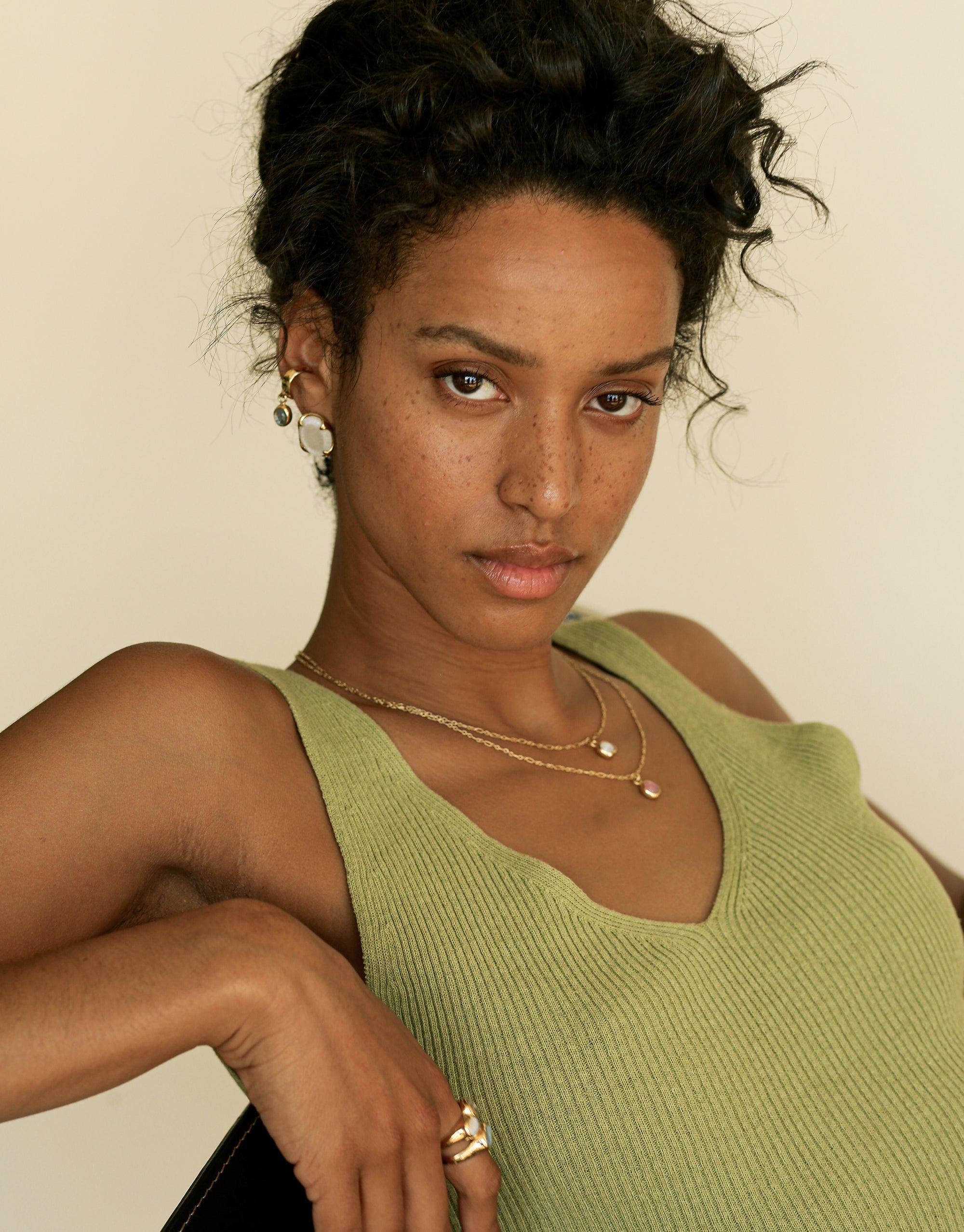 Elegant oval dangling ear cuff showcased on model wearing green top and delicate necklaces. Handcrafted jewelry piece with eco-friendly charm made from upcycled glass. Stylish and sustainable accessory for everyday wear. Oval Dangling Ear Cuff by CLED.