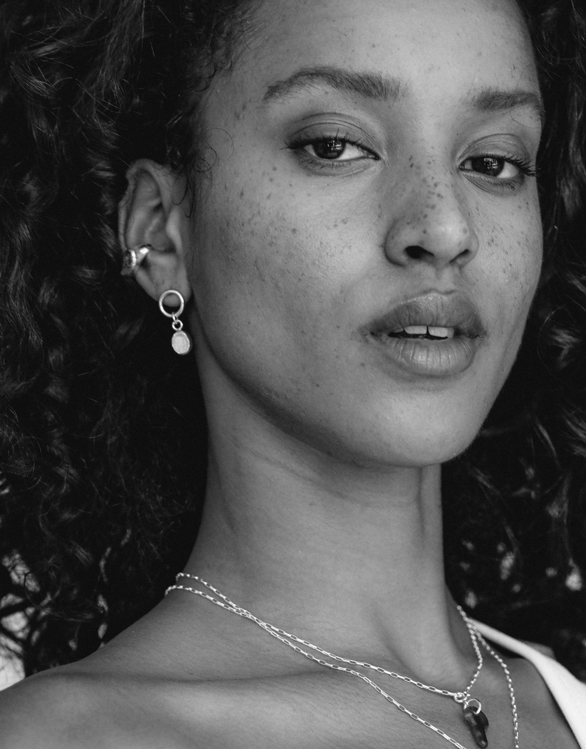 Close-up black and white portrait showcasing Oval Dangling Earrings with delicate charm, highlighting elegant design and subtle facial features. Necklace visible, complementing earring style. Handcrafted jewelry by CLED.