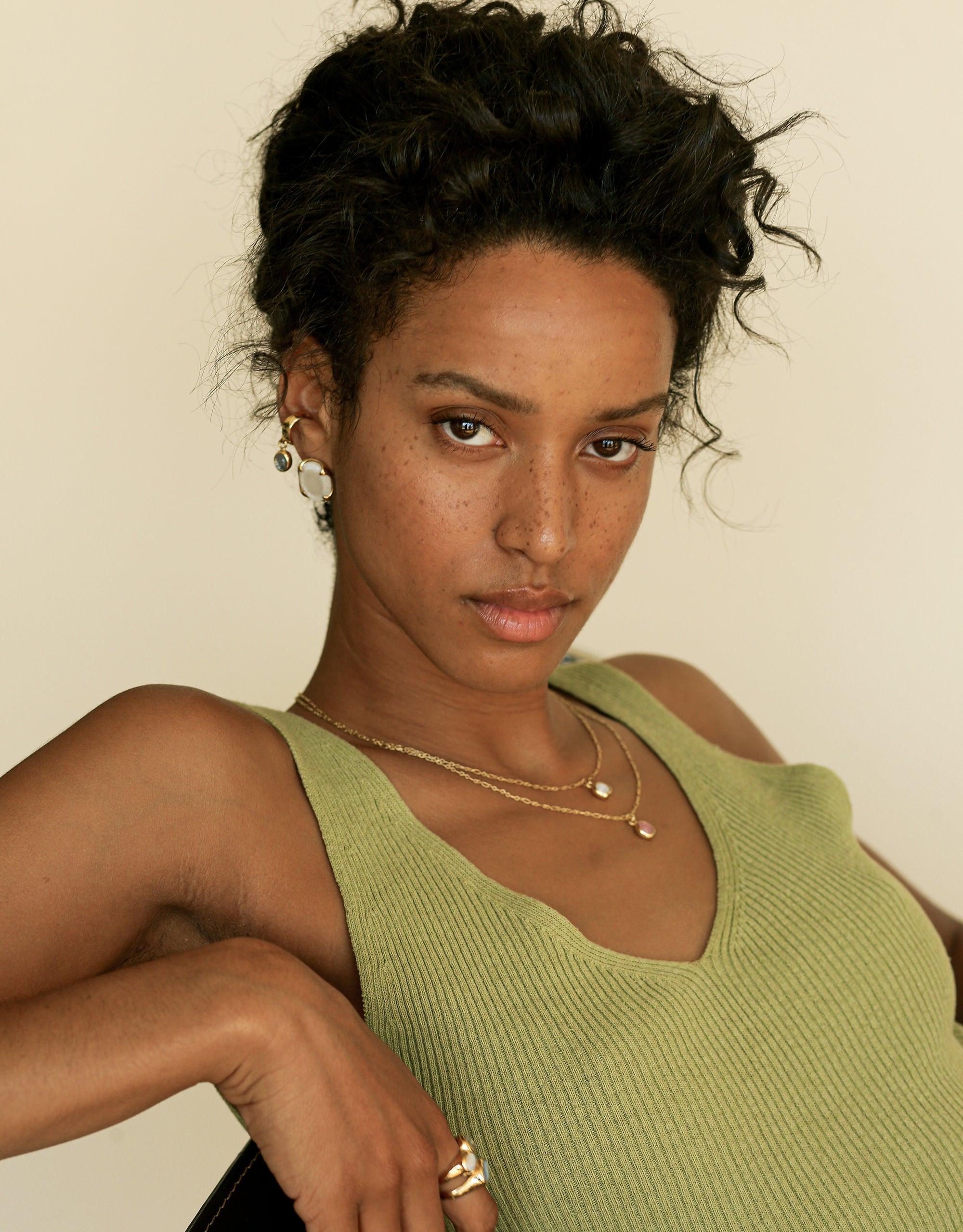 Close-up of model wearing green sleeveless top and delicate layered necklaces, showcasing Oval Charm Necklace. Elegant jewelry design with adjustable chain length and eco-friendly charm. Handcrafted sustainable accessory by CLED.