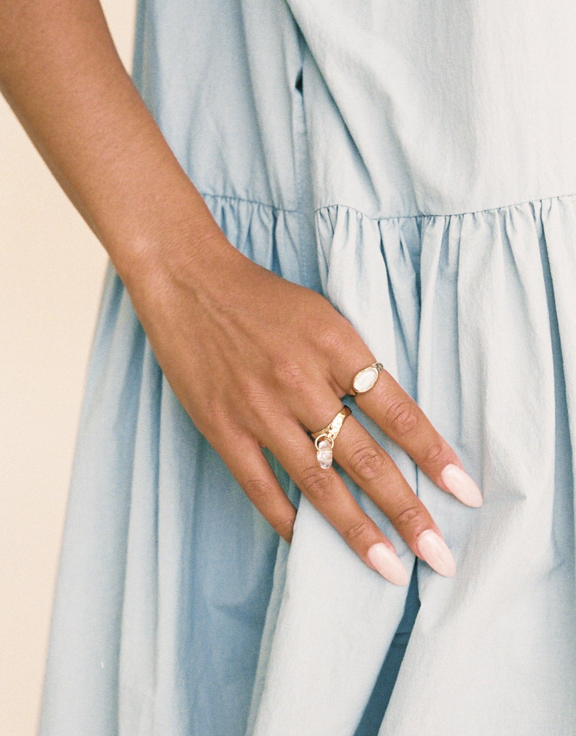 Elegant hand modeling Donut Dangling Ring, showcasing delicate jewelry against light blue dress fabric. Unique eco-friendly design highlighting sustainable fashion and handmade craftsmanship. Perfect accessory for conscious consumers seeking stylish, environmentally responsible jewelry. CLED, Donut Dangling Ring.