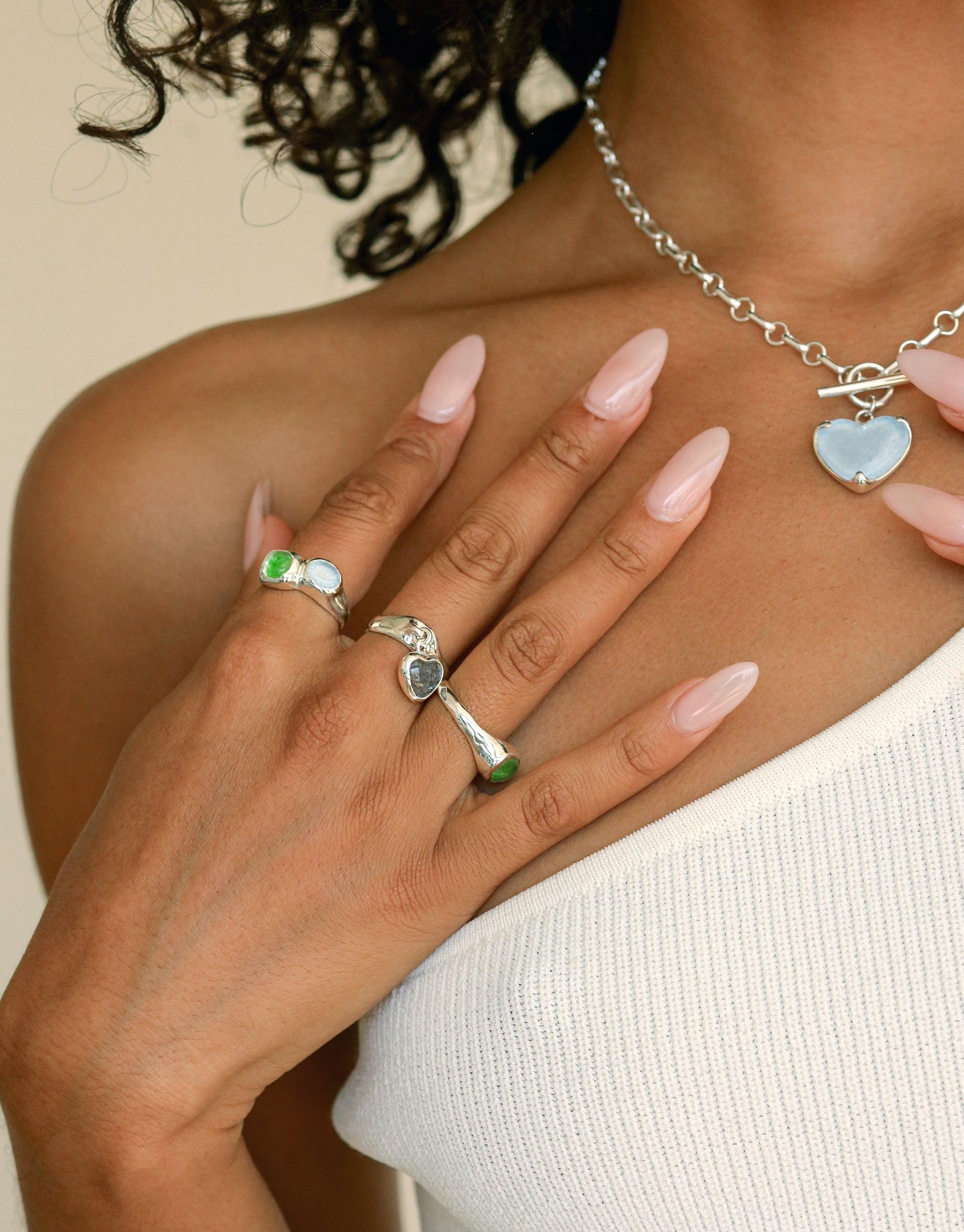 Elegant hand wearing Heart Dangling Ring and other eco-friendly jewelry pieces. Silver chain necklace with heart pendant. Sustainable fashion accessory showcasing unique designs and upcycled materials. Handmade jewelry by CLED.