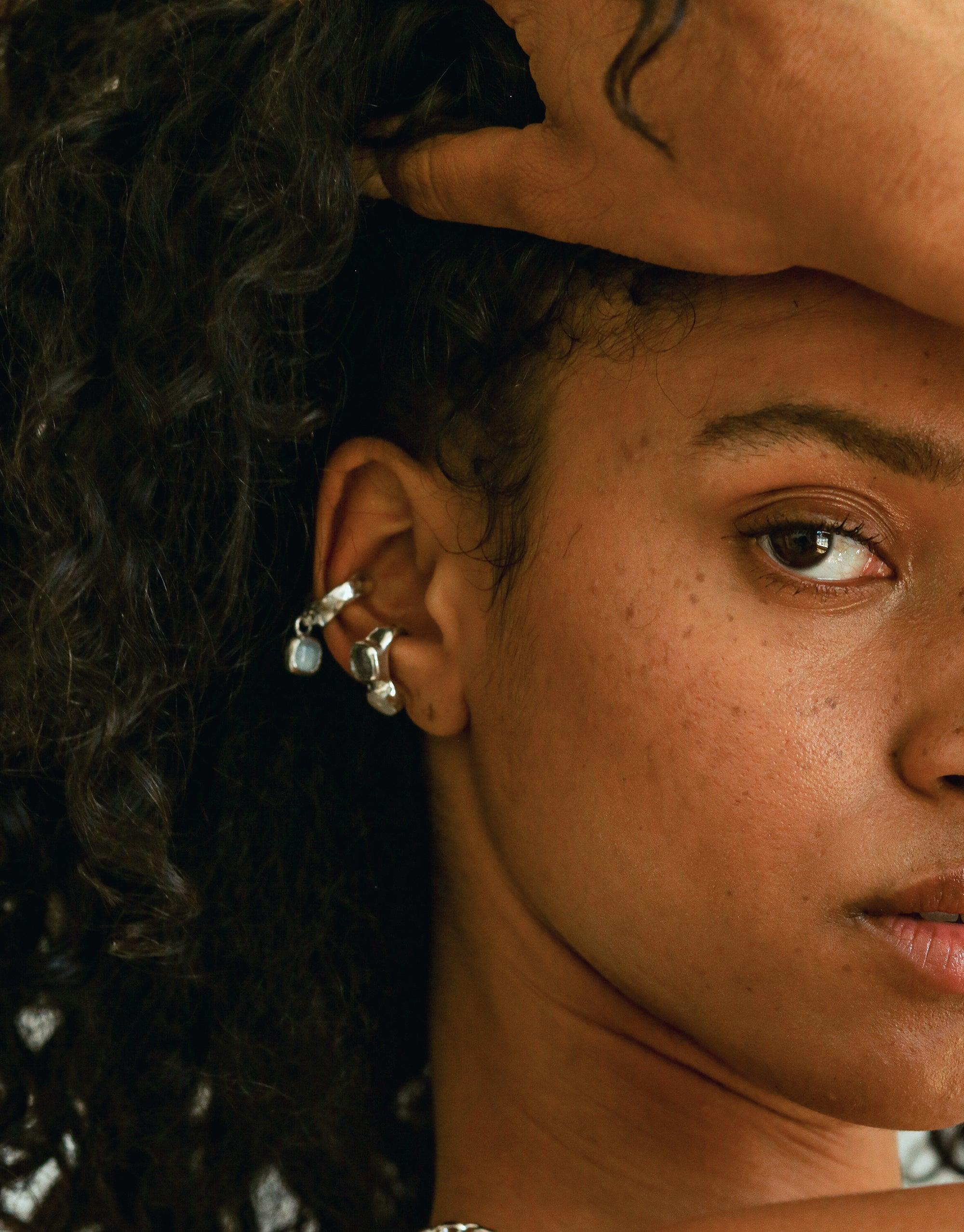 Close-up of an ear adorned with the Duo Sculpture Ear Cuff, featuring delicate charms and a unique design. The cuff showcases intricate metalwork and upcycled glass elements, highlighting its handcrafted nature. Duo Sculpture Ear Cuff by CLED