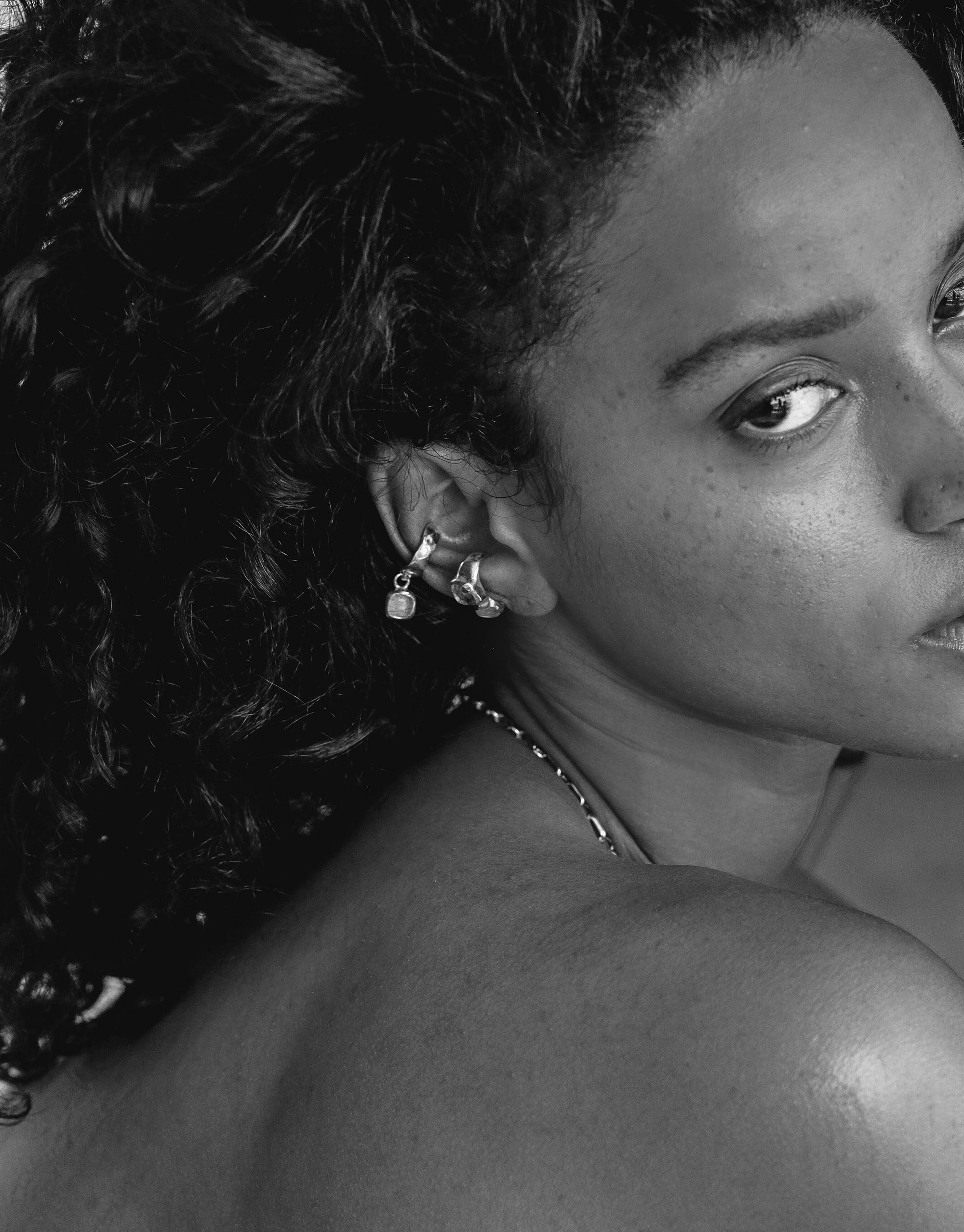 Close-up black and white image showcasing the Duo Sculpture Ear Cuff, highlighting its unique design on a model's ear. The cuff features intricate charm details, exemplifying handcrafted artistry. Sustainable jewelry by CLED, Duo Sculpture Ear Cuff.