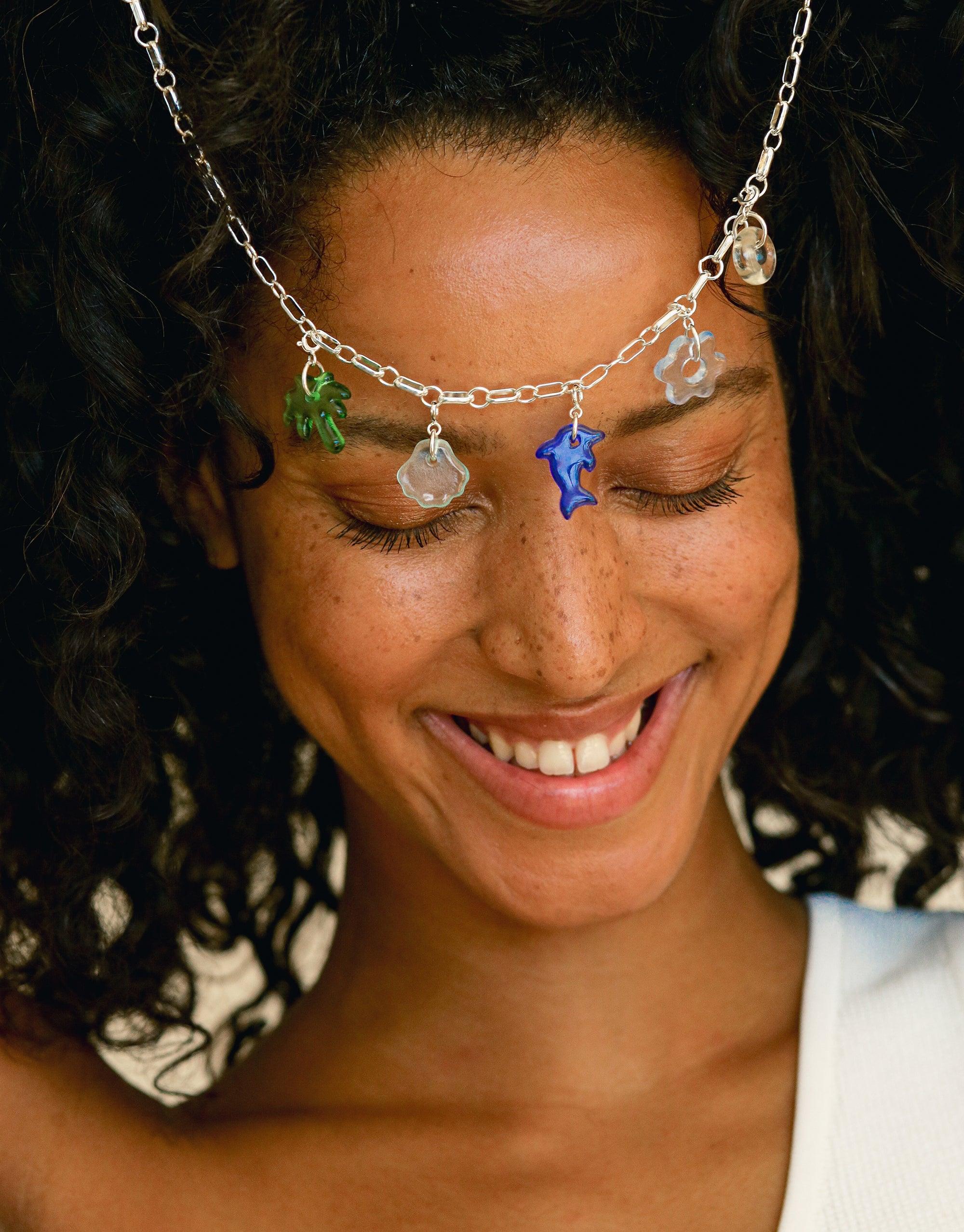 Delicate silver chain necklace adorned with colorful glass charms, including a green leaf, clear crystal, blue star, and silver flower. Showcasing the Avens | Icon Charm collection's versatile and eco-friendly design. Handcrafted jewelry by CLED.