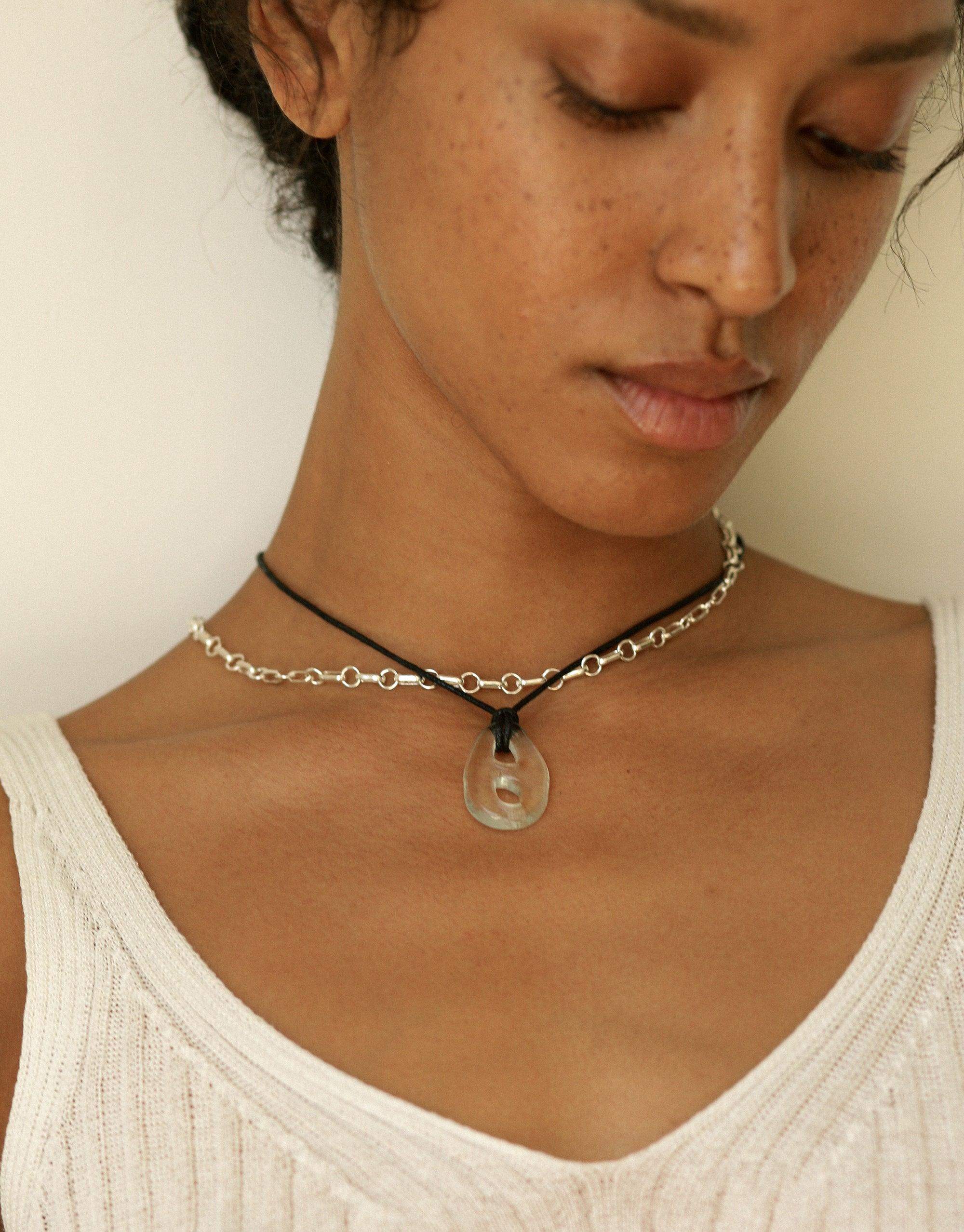 Close-up of Sculptural Small Charm Necklace | B featuring a delicate cotton cord with silver chain and upcycled glass pendant. The necklace rests elegantly on a model's neck, showcasing its unique design and eco-friendly materials. Handcrafted jewelry by CLED.