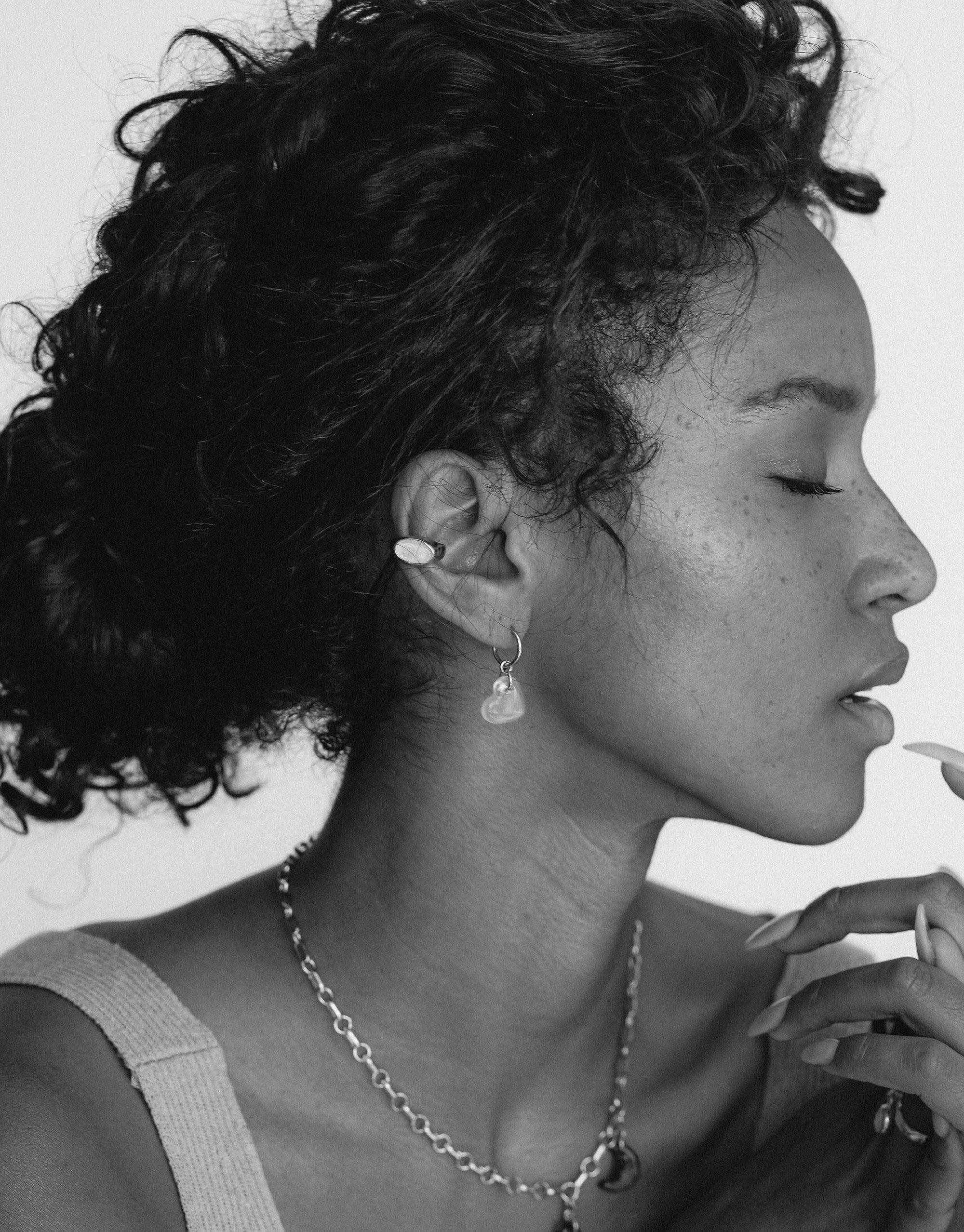 Profile view of a person wearing an Oval Sculpture Ear Cuff, showcasing its elegant design. Curly hair frames the face, highlighting the unique jewelry piece. Black and white image emphasizes the sculpted form of the cuff. Handmade sustainable accessory by CLED.