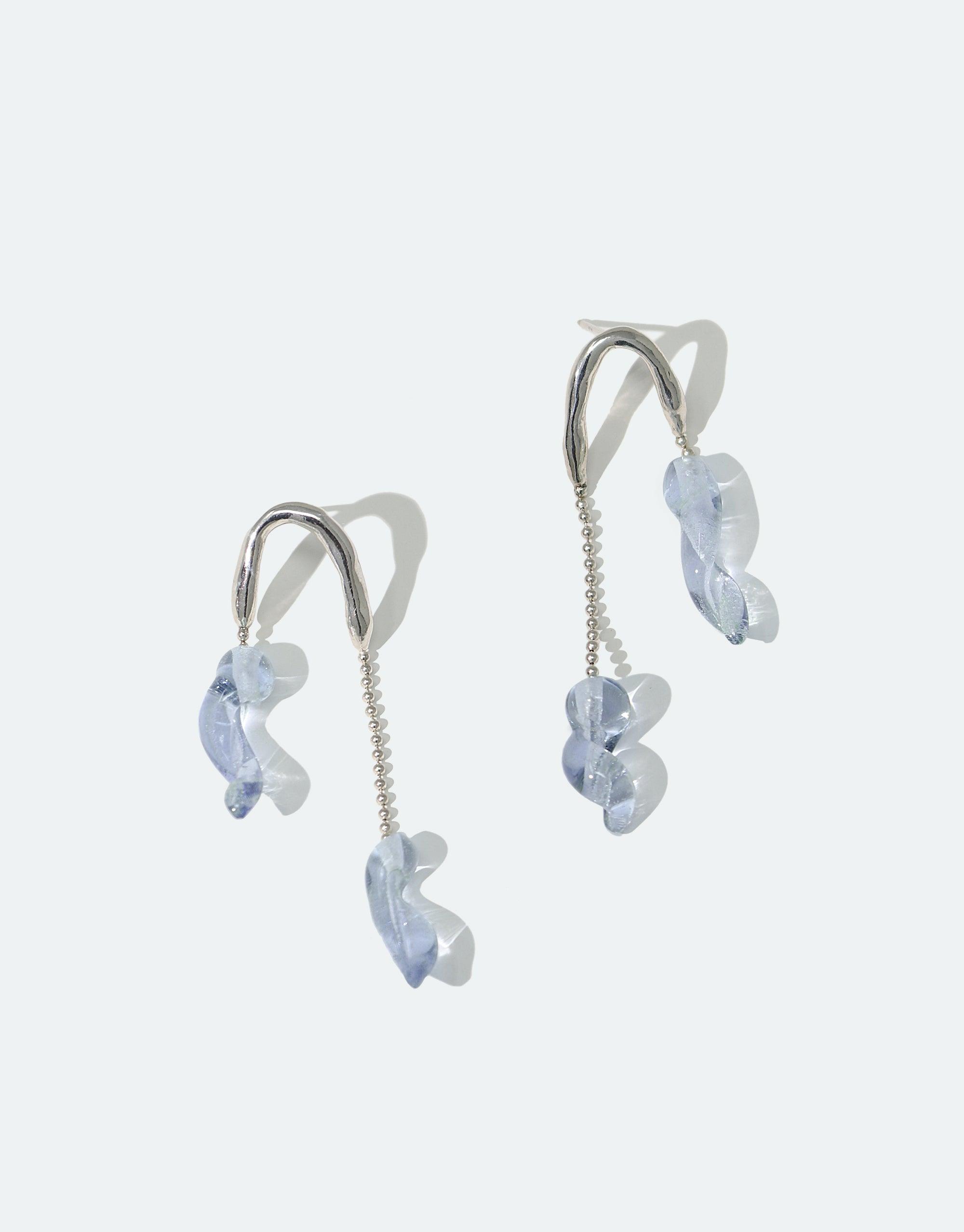 Asymmetrical silver earrings with delicate light blue glass drops resembling icicles, showcasing elegant design and eco-conscious craftsmanship. Crystal Drops Earrings from the Floating Glacier Collection by CLED.