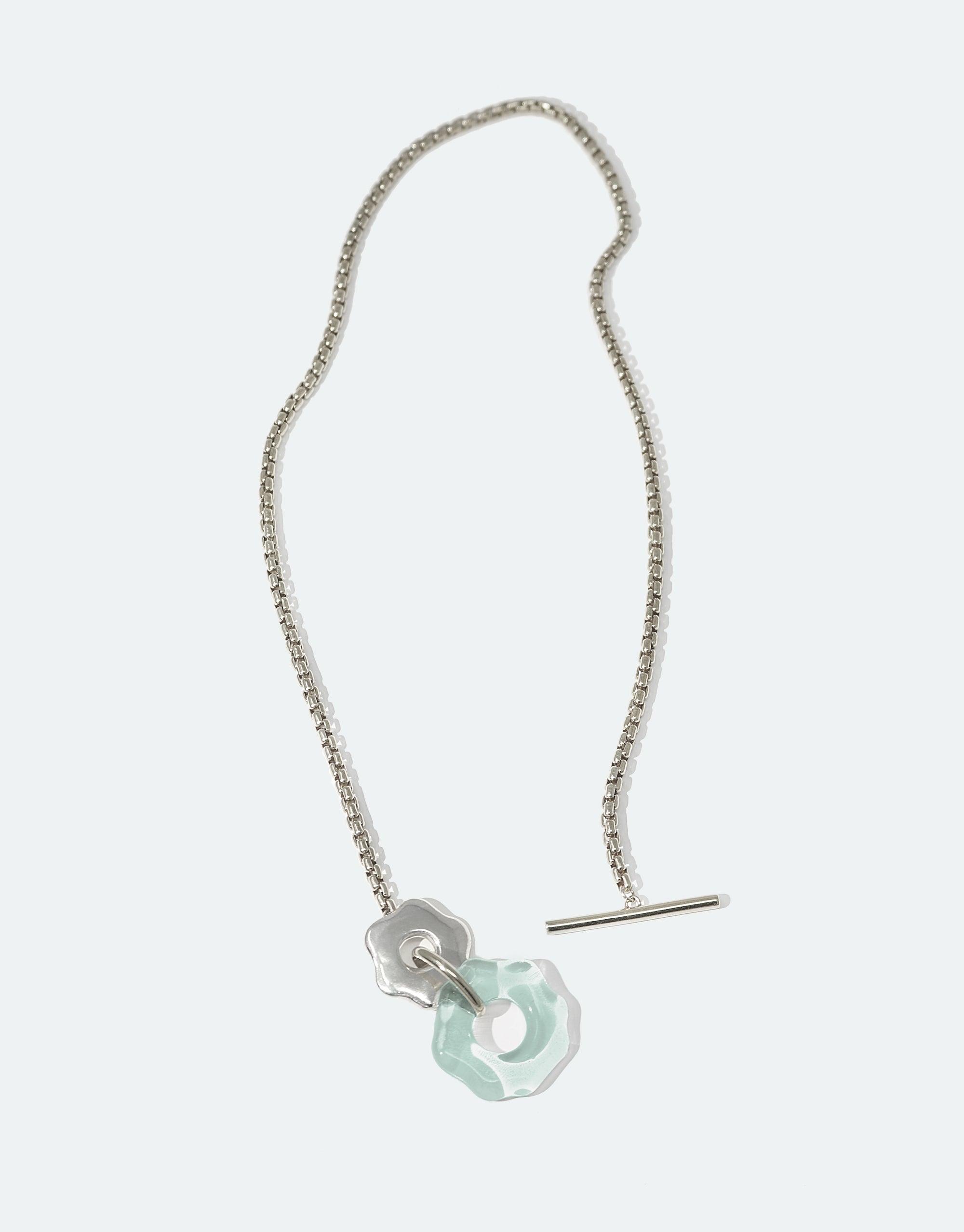 Elegant Avens Toggle Necklace featuring a silver chain with a light blue glass pendant and metal flower-inspired toggle closure. Sustainable jewelry design inspired by Arctic flora. CLED