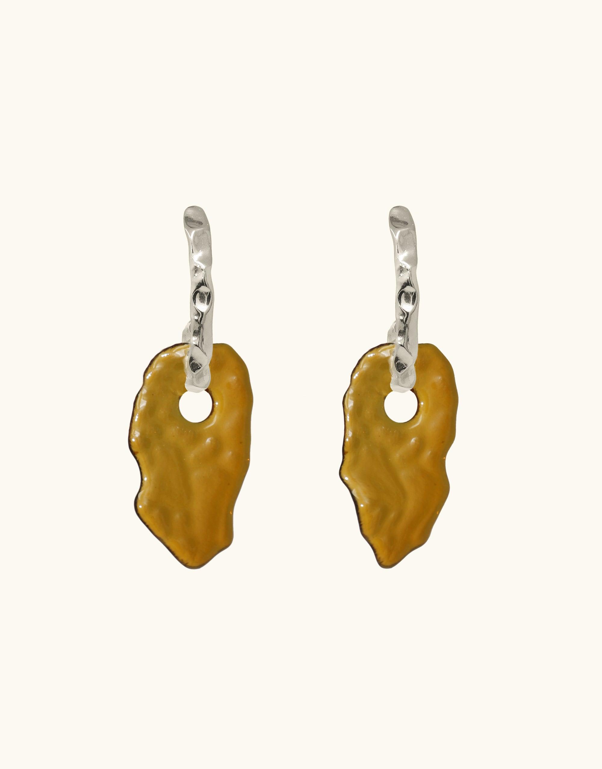 Rock Spire Earrings featuring silver curved hooks with amber-colored glass drops. Unique, hand-formed eco-friendly jewelry inspired by canyon terrain. Statement earrings showcasing abstract molten forms and layers, representing distinct canyon formations. Handmade sustainable accessories by CLED.