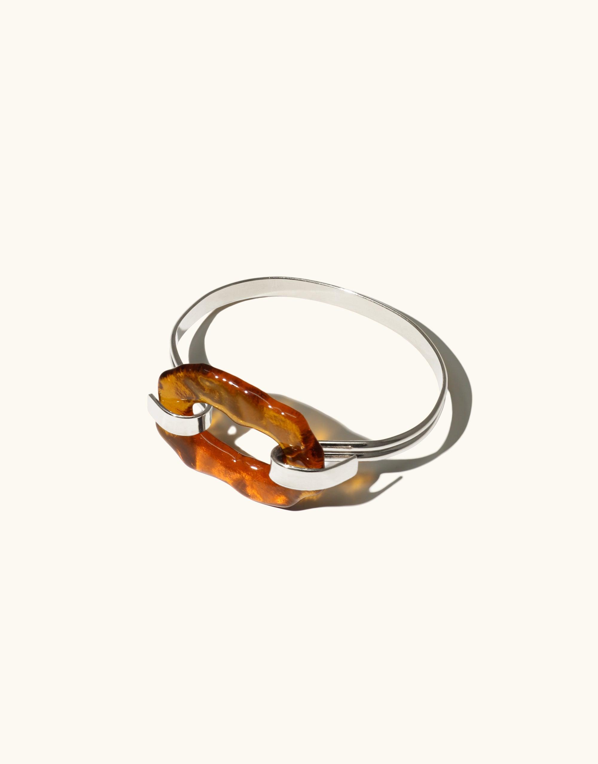 Elegant Canyon Hook Bracelet featuring a smooth oval shape with double bands and an amber-colored eco gem repurposed from glass bottles, set against a white background. Handcrafted sterling silver design inspired by canyon terrain. CLED Canyon Hook Bracelet.