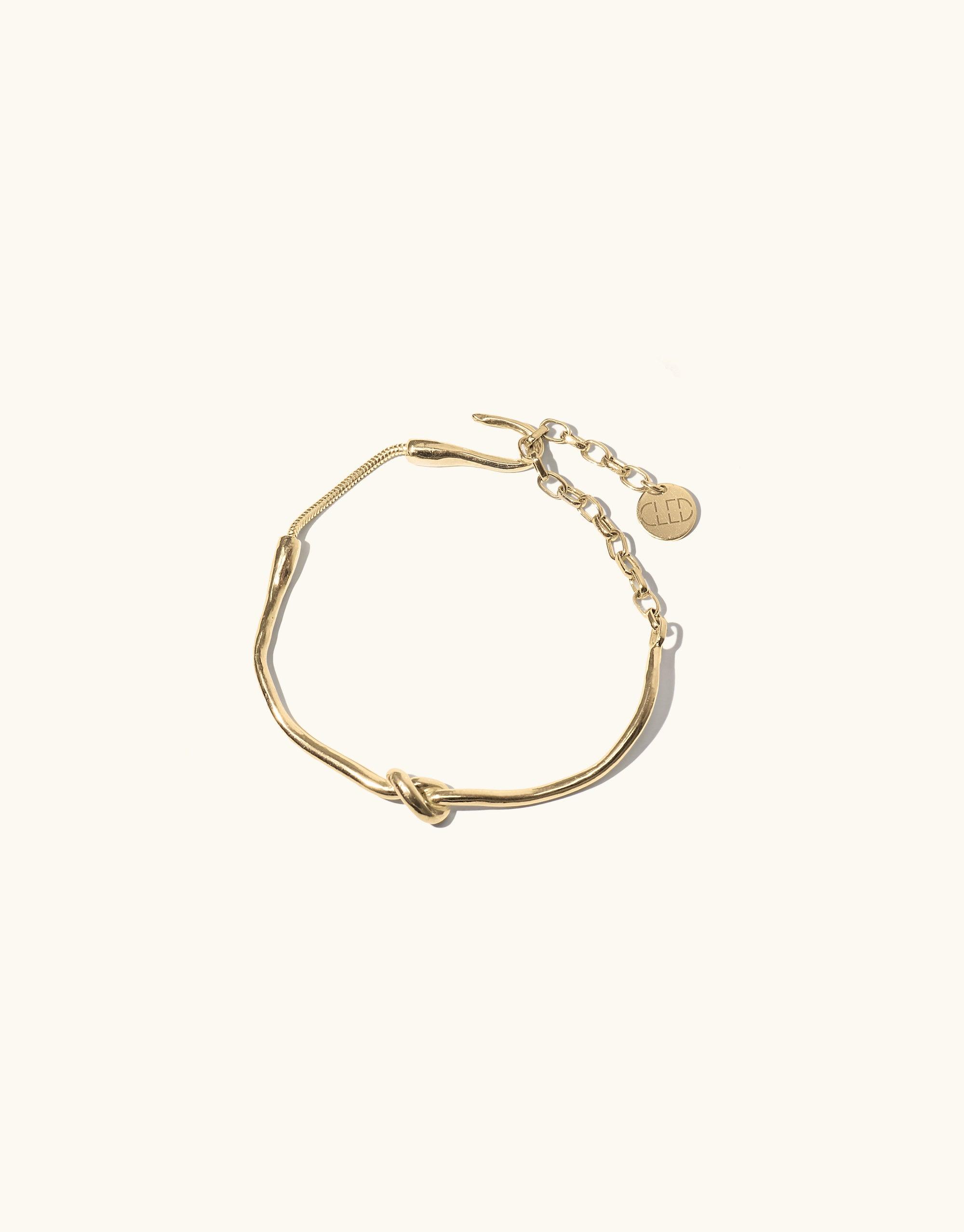 Gold-toned Single Rope Hook Bracelet with knotted design, chain closure, and brand charm. Elegant and minimalist accessory inspired by canyon terrain. Handcrafted piece from the Terrain Collection. CLED Single Rope Hook Bracelet.