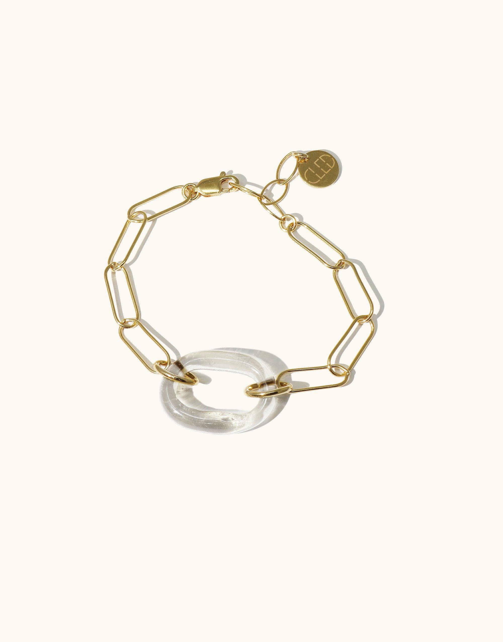 The Day Loop Bracelet features a gold oval chain with a white Eco Gem circle and gold tag, hand-formed from repurposed glass, embodying CLED's eco-conscious craftsmanship.