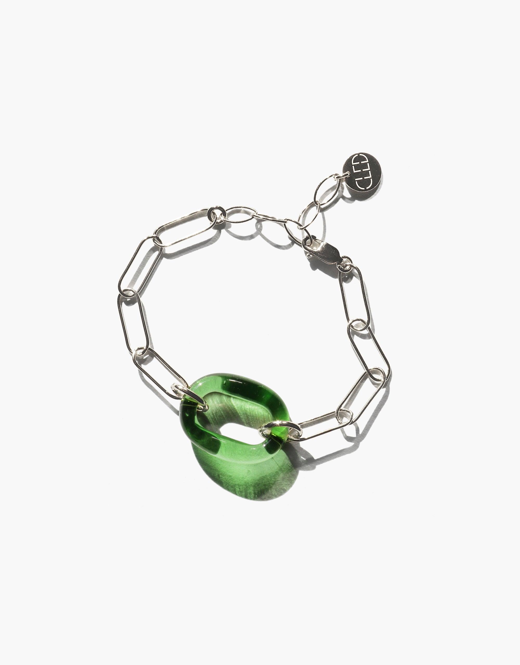 The Day Loop Bracelet, featuring a green Eco Gem and silver oval chain links, is a minimalist statement piece, crafted from repurposed glass, reflecting CLED's eco-conscious jewelry ethos.