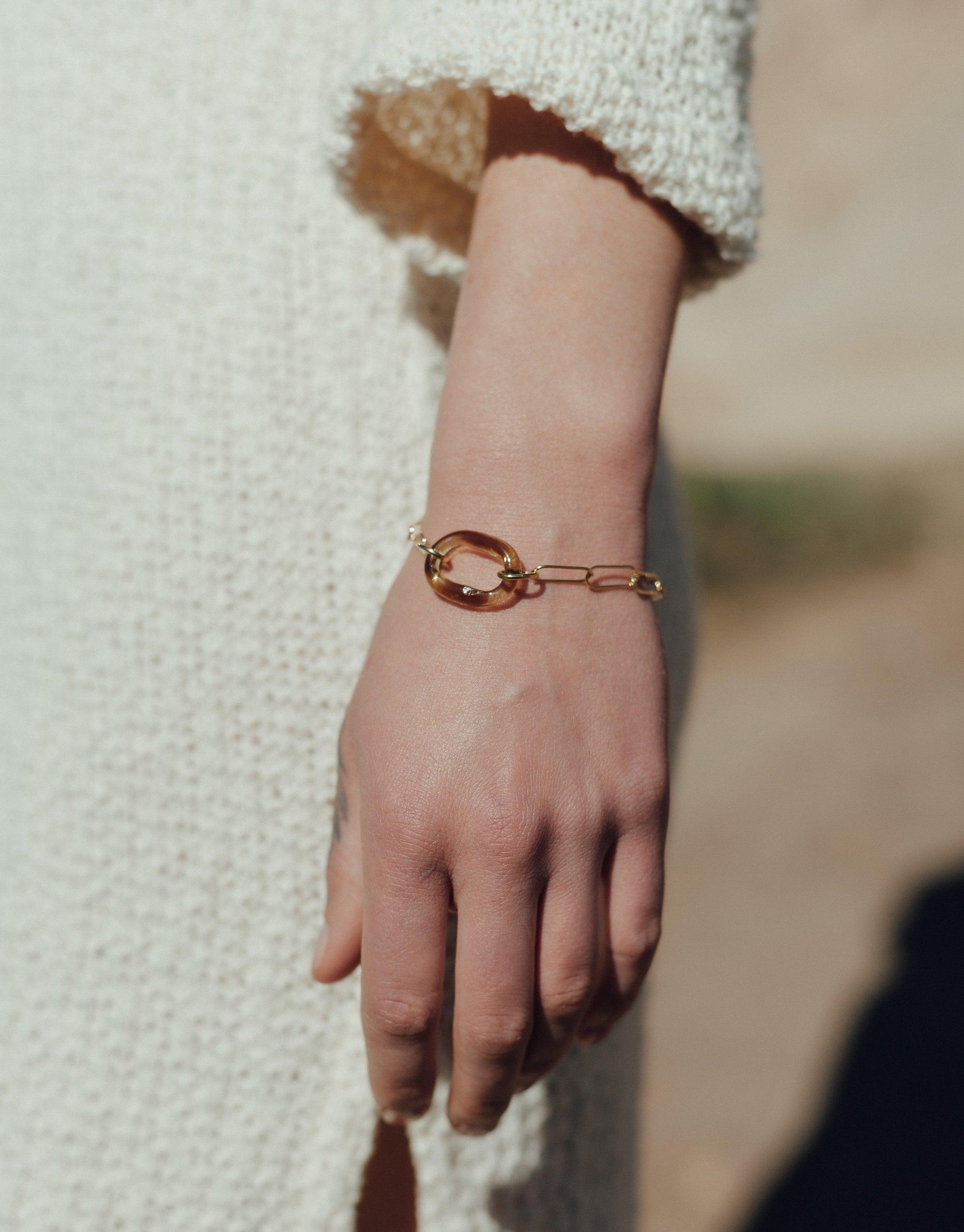The Day Loop Bracelet features an elegant oval chain, beautifully displayed on a hand. This minimalistic piece exemplifies eco-conscious craftsmanship from CLED, made from repurposed glass.