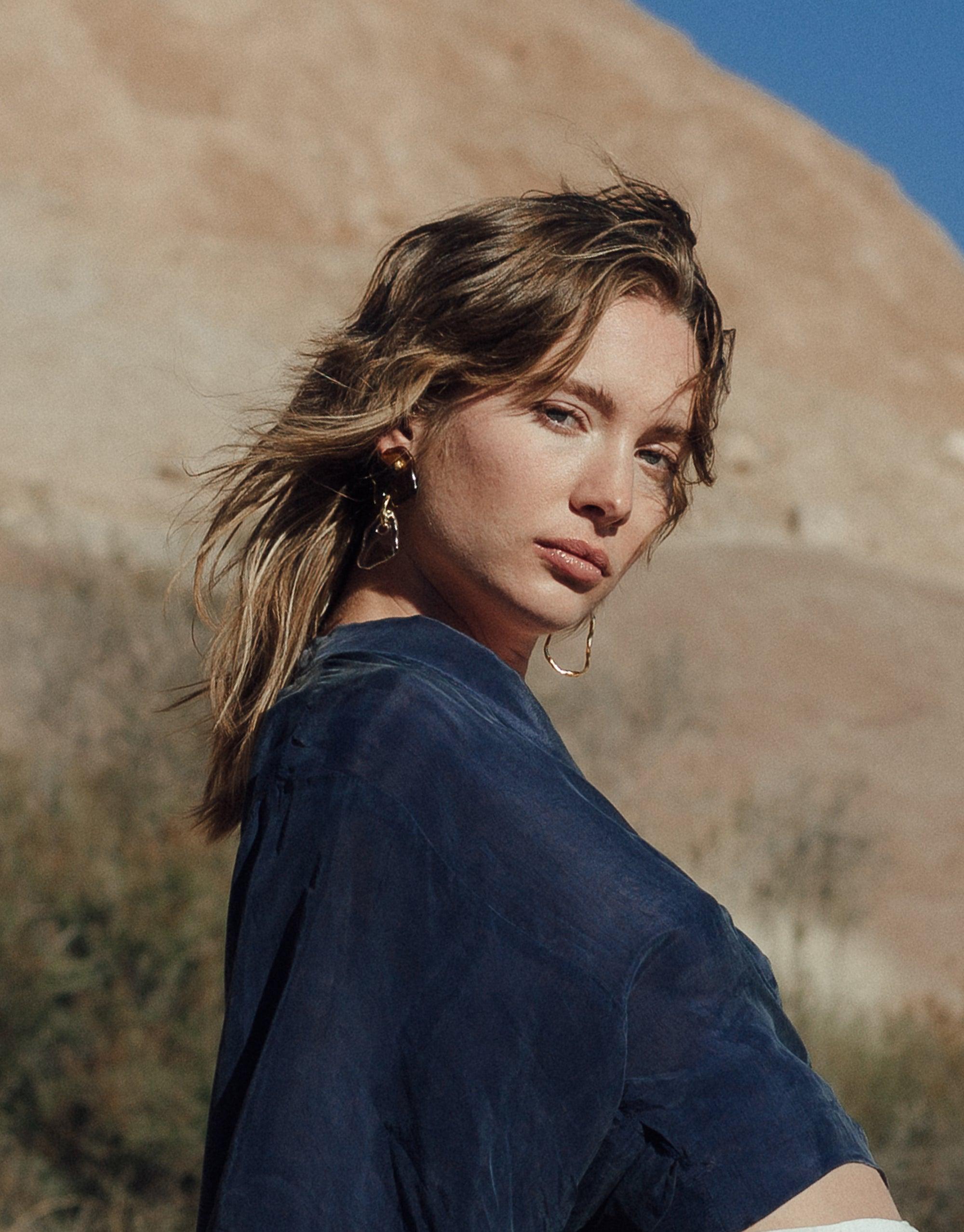 Model wearing Peak Earrings from Terrain Collection against canyon backdrop, showcasing layered glass charms inspired by mountain formations. Handcrafted eco-friendly jewelry made from repurposed glass bottles. Sustainable and stylish accessory by CLED.