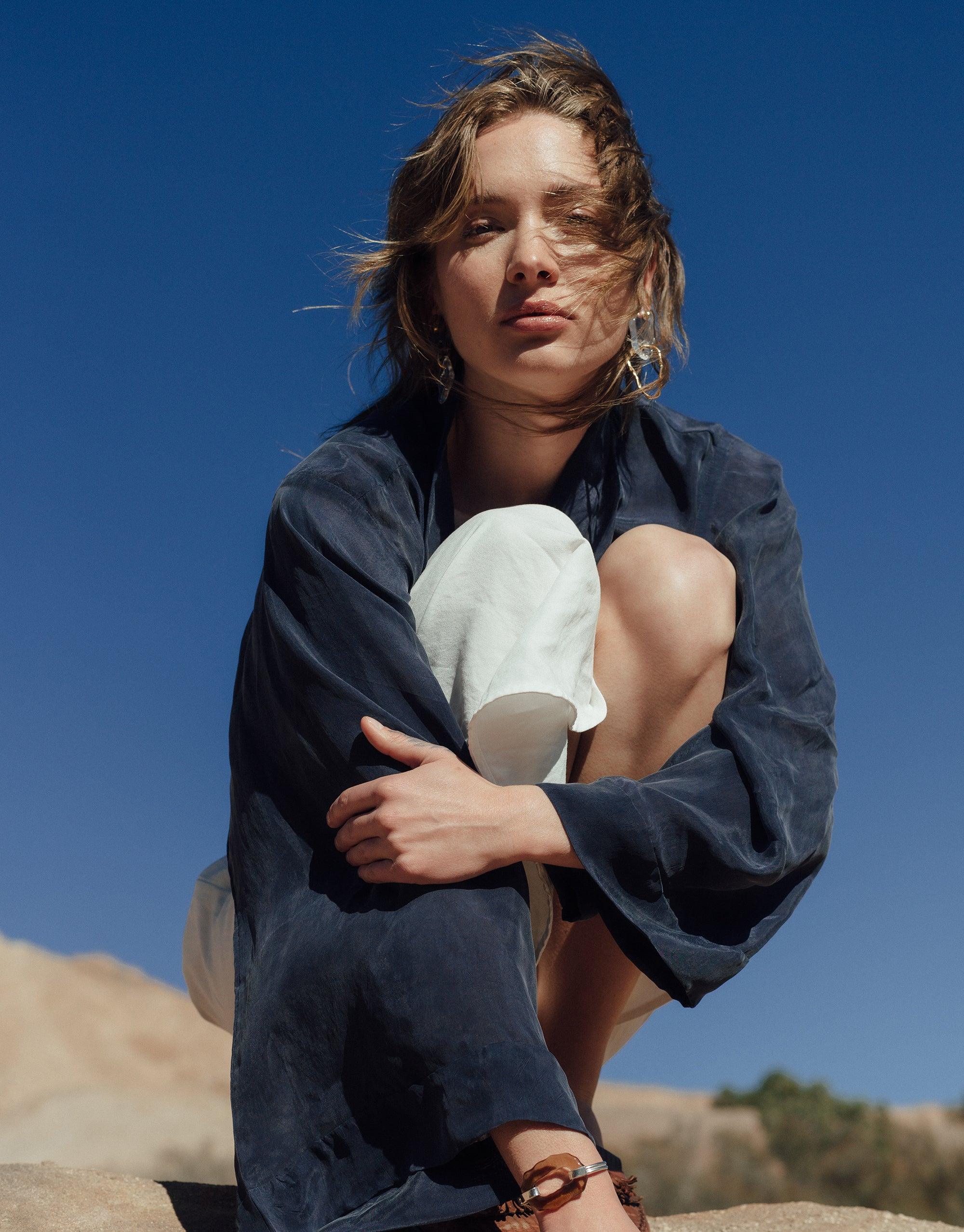 Model wearing Peak Earrings from Terrain Collection against blue sky and desert backdrop. Long, layered glass charms visible, inspired by canyon formations. Handmade eco-friendly jewelry showcasing abstract molten forms and repurposed glass. Sustainable fashion statement by CLED. Peak Earrings.