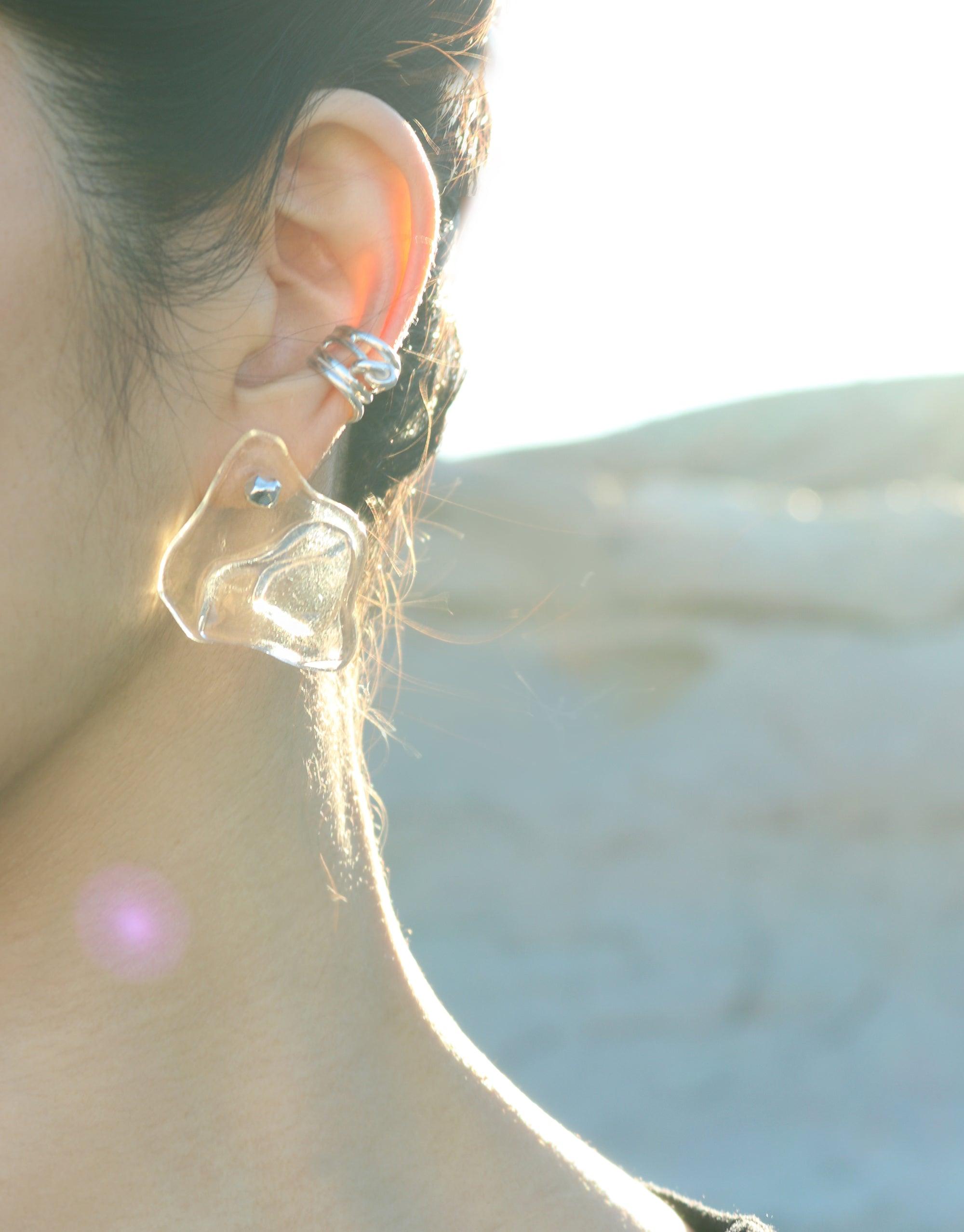 Close-up of a person wearing Plateau Earrings, showcasing the unique glass design inspired by canyon terrain. Sunlight illuminates the earring, highlighting its translucent and organic form. Handcrafted eco-friendly jewelry by CLED.