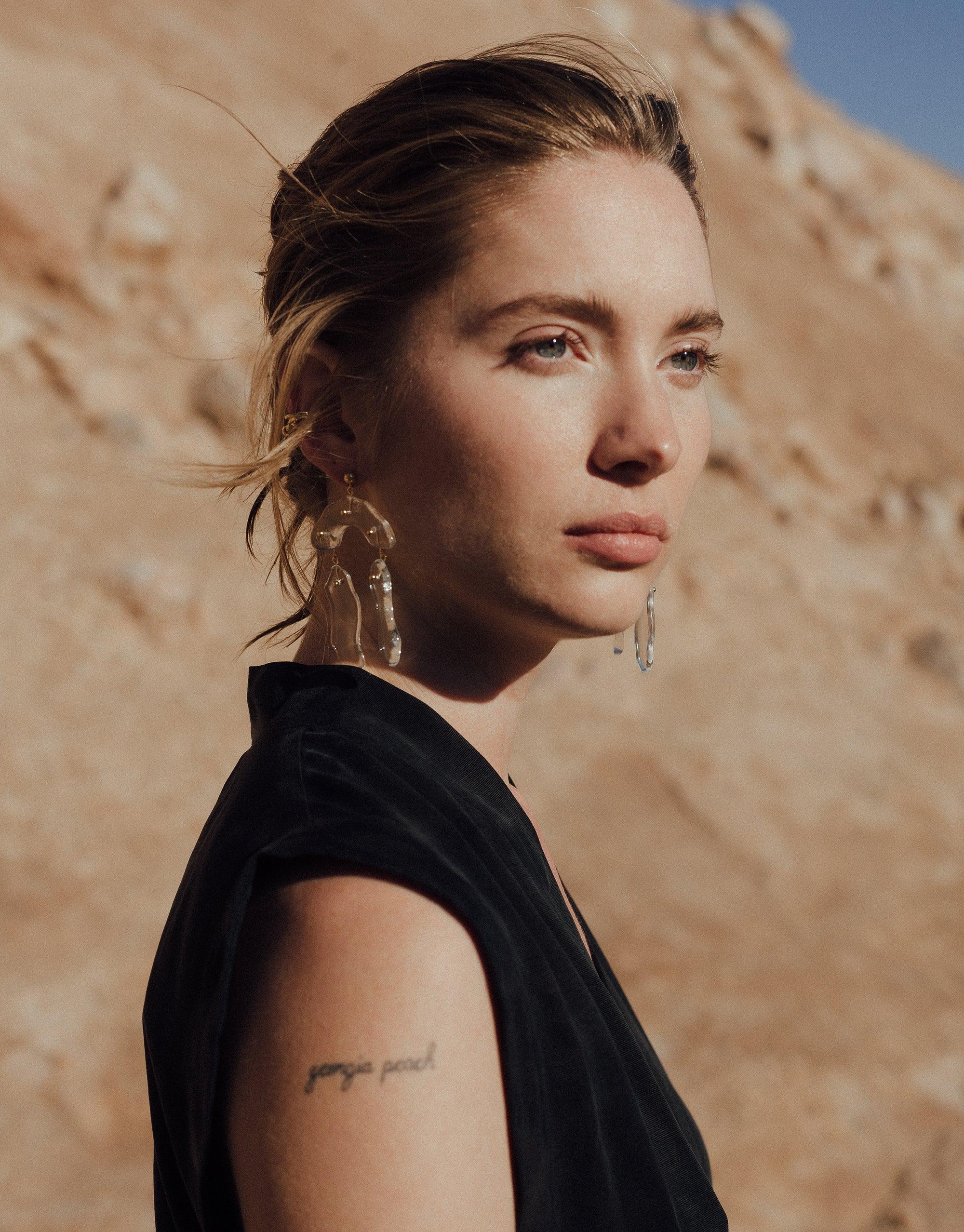 Elegant model wearing Rock Dangling Earrings against canyon backdrop, showcasing handcrafted eco-friendly jewelry inspired by terrain formations. Sustainable fashion accessory with abstract molten forms and layers of glass. Rock Dangling Earrings by CLED