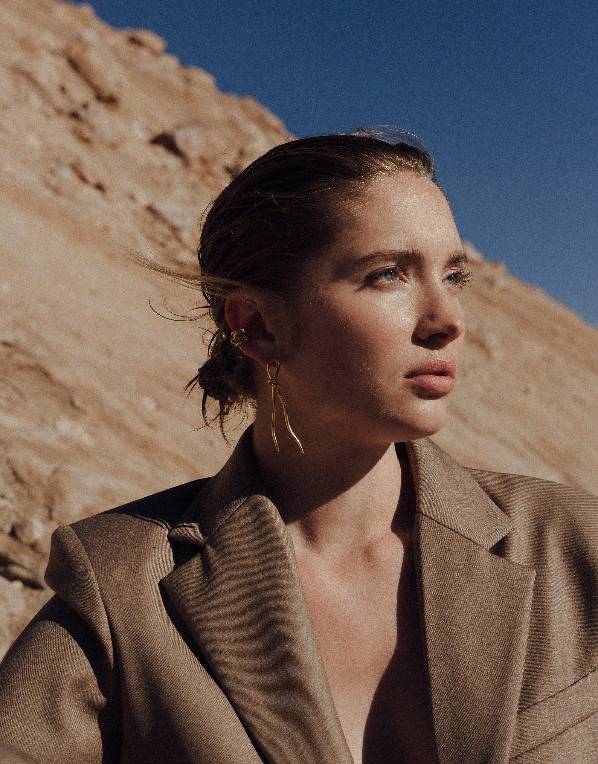 Woman wearing Rope Earrings in desert landscape, showcasing unique canyon-inspired design. Stylish gold vermeil earrings complement natural terrain backdrop, highlighting Terrain Collection's aesthetic. Handcrafted jewelry by CLED, Rope Earrings.