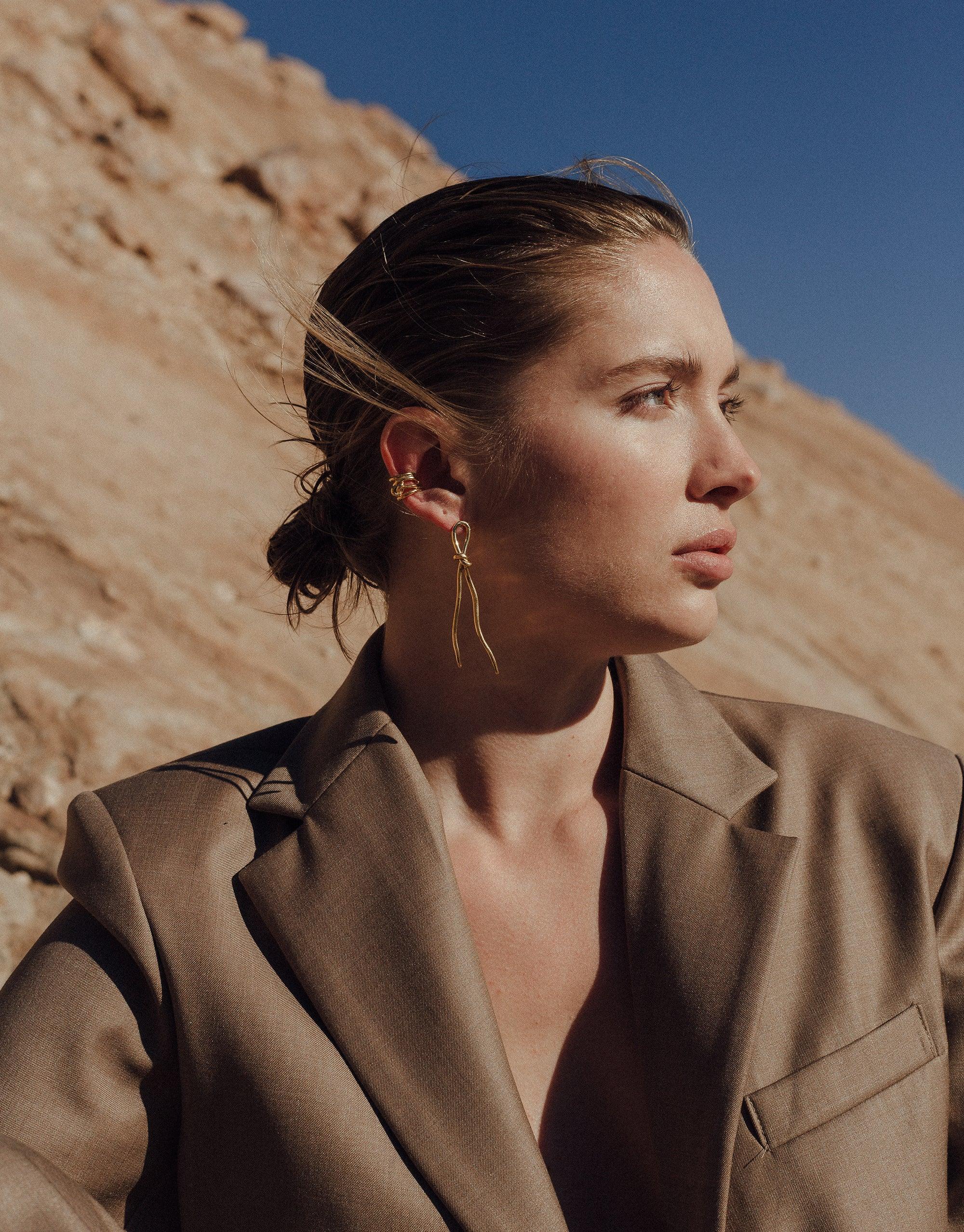 Model wearing Rope Ear Cuff, part of the Terrain Collection, showcasing its sleek design against desert canyon backdrop. Elegant gold vermeil accessory complementing tan blazer. Handcrafted jewelry inspired by canyon formations. Rope Ear Cuff | Single by CLED
