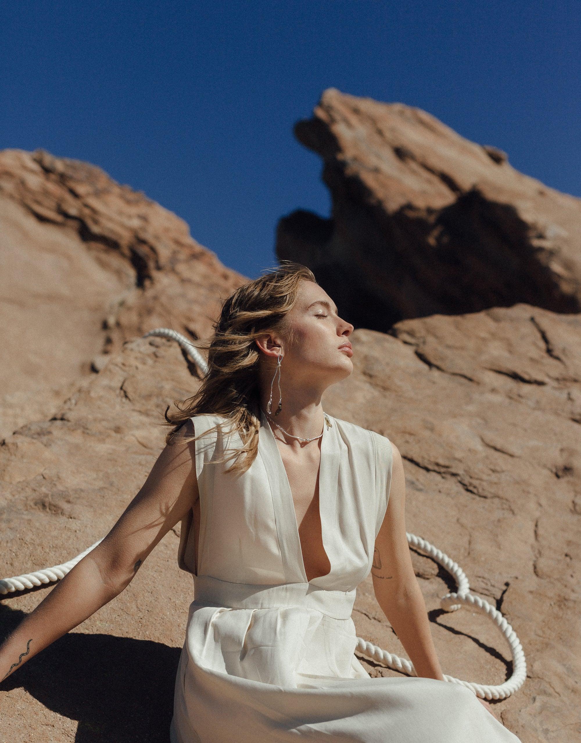 Woman in white dress against canyon backdrop, wearing Rope Drop Earrings. Earrings feature abstract shapes inspired by rock climbing ropes and eco-friendly glass drops, embodying the Terrain Collection's canyon-inspired design. Handcrafted jewelry by CLED.
