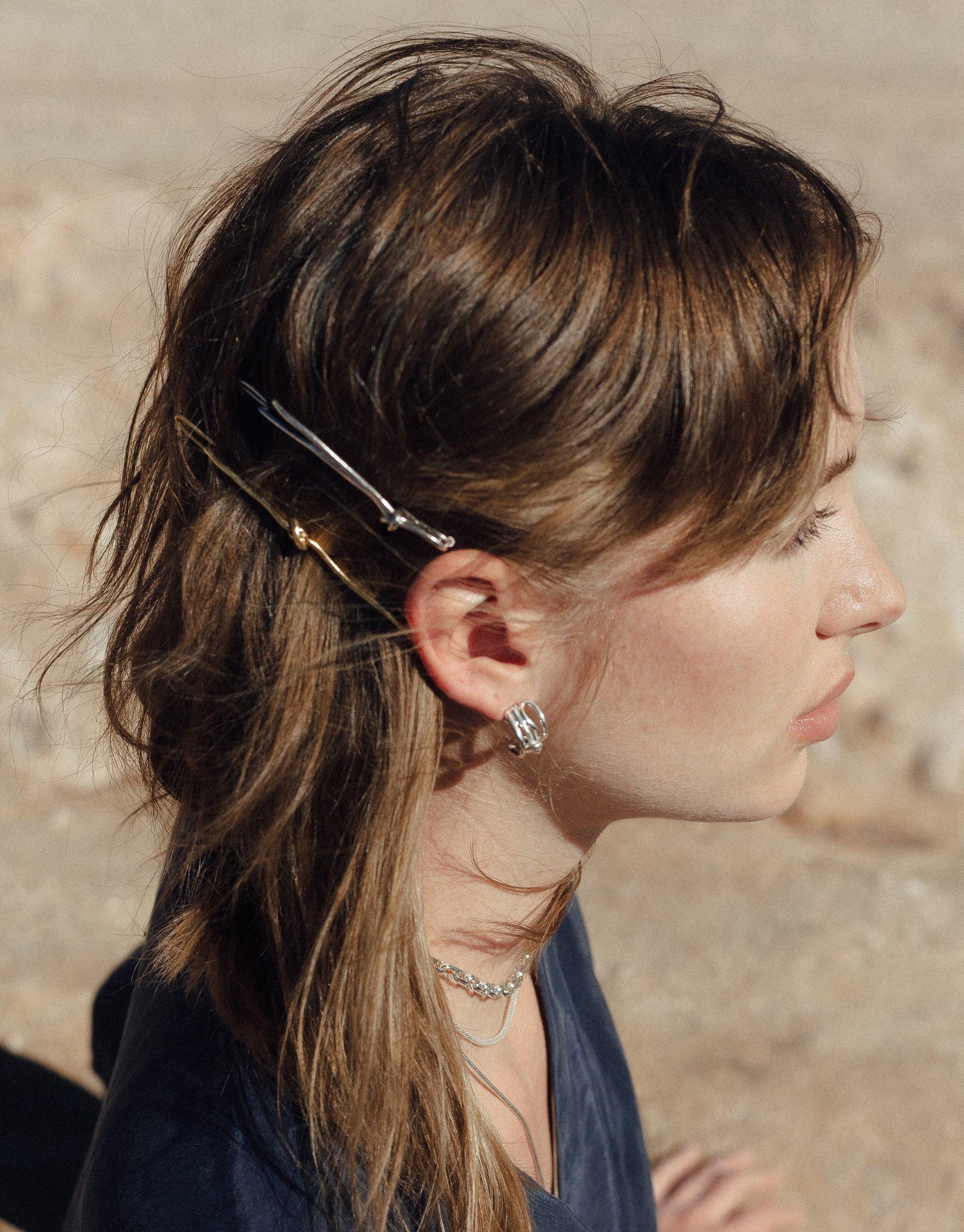 Elegant Single Rope Hair Barrette in silver and gold tones, showcasing abstract molten forms inspired by canyon terrain, worn in brown hair against a desert backdrop. Handcrafted accessory from the Terrain Collection by CLED.