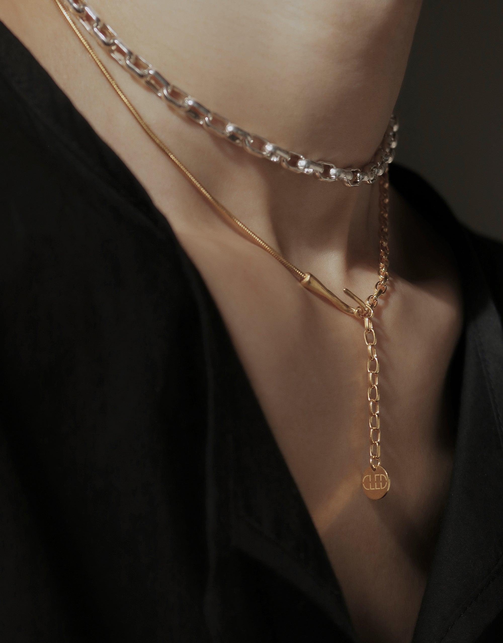 Close-up of layered necklaces, featuring a delicate gold chain with a hook pendant and a silver link chain, showcasing the versatile Rope Hook Necklace design inspired by canyon terrain. Elegant and adaptable jewelry piece by CLED.