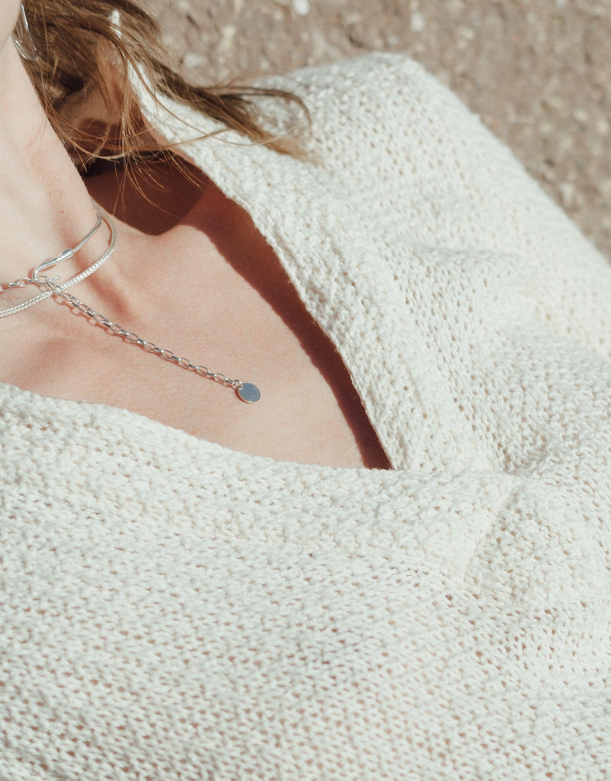 Close-up of a person wearing a white knit sweater and a delicate silver chain necklace with a small pendant, showcasing the Rope Hook Necklace's versatile and elegant design. Inspired by canyon terrain, perfect for layering. CLED Rope Hook Necklace.