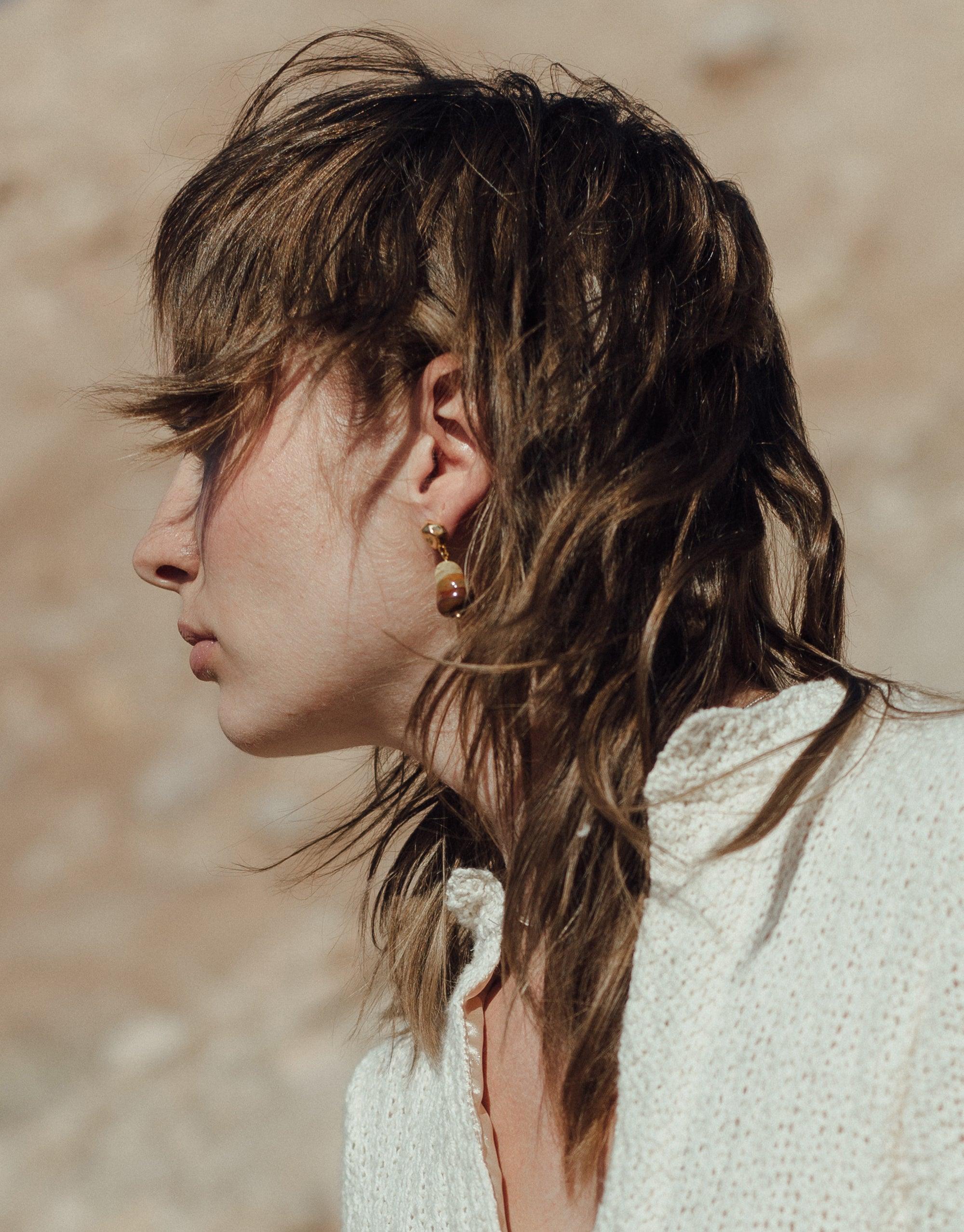 Profile view of a person wearing Shades of Nature Sandstone Earrings, showcasing the elegant design inspired by canyon terrain. The earrings feature abstract molten forms and layers of glass, reflecting the colors of nature's landscape. Handcrafted eco-friendly jewelry by CLED.