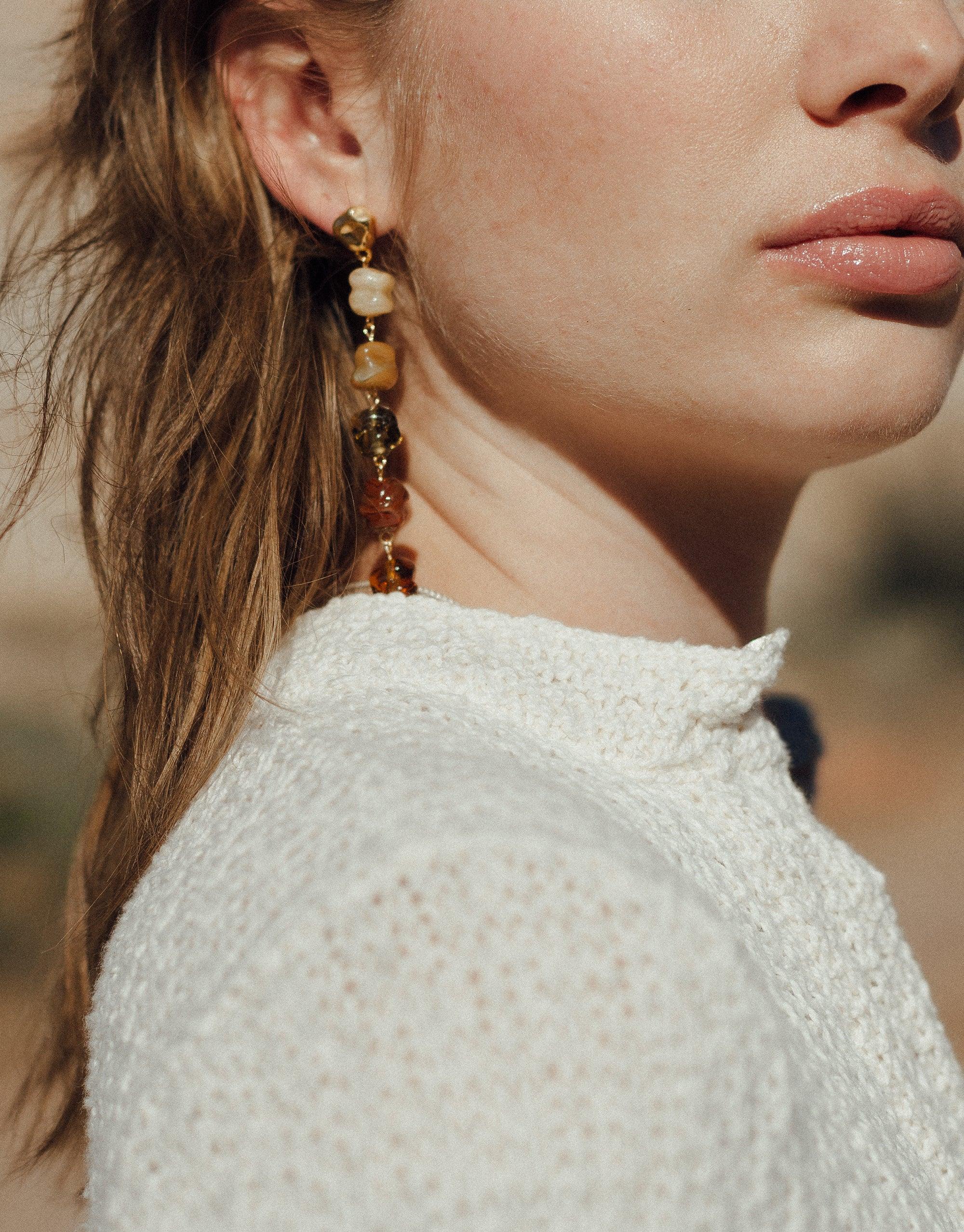 Elegant Shades of Nature Sandstone Earrings showcasing long, dangling design with warm-toned glass beads inspired by canyon terrain. Worn by model in white lace top, highlighting eco-friendly luxury jewelry. Handcrafted sustainable accessory by CLED.