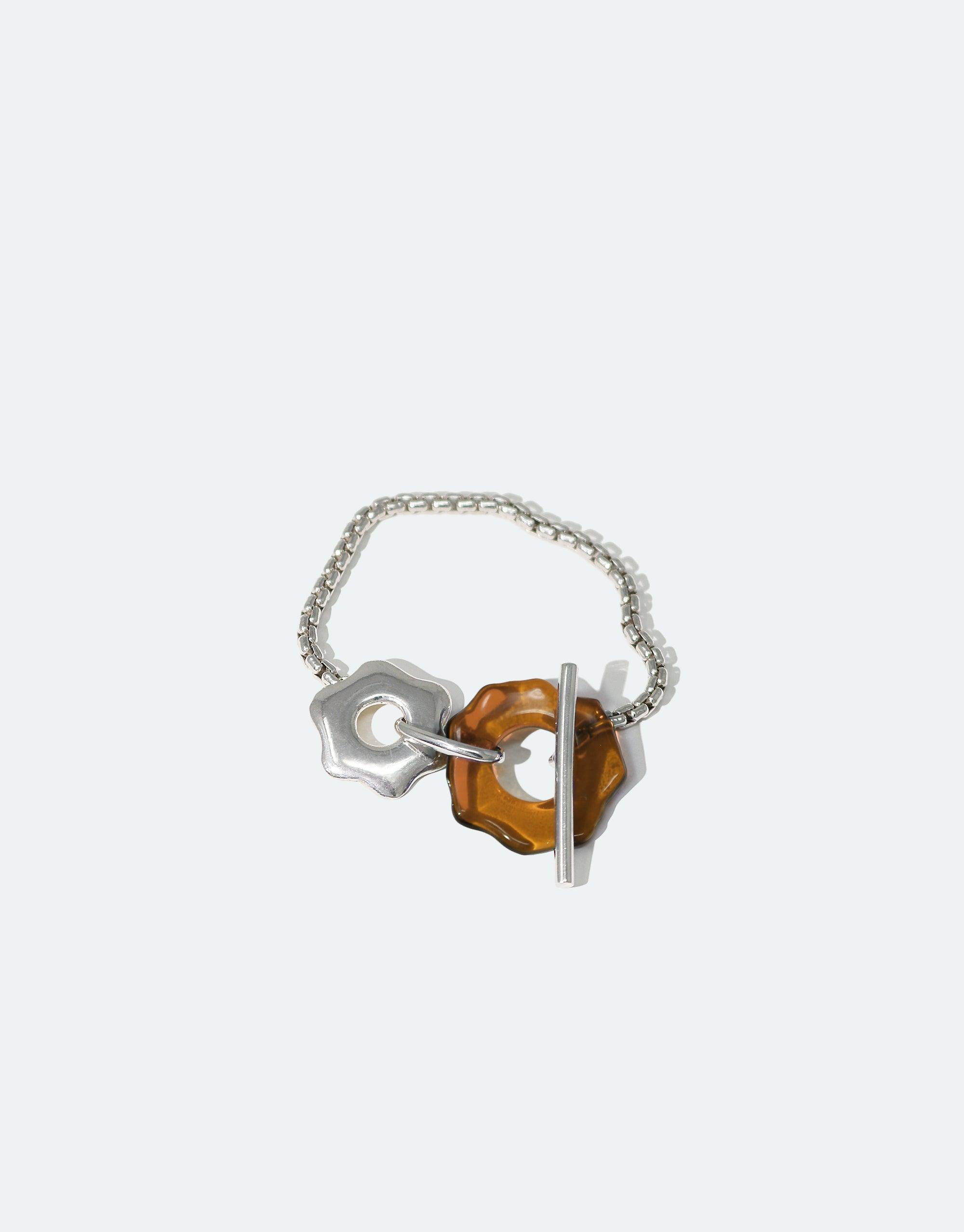 Avens Toggle Bracelet featuring a silver chain with unique flower-inspired toggle clasp and amber-colored eco gem made from recycled glass. Elegant and environmentally conscious jewelry design by CLED.