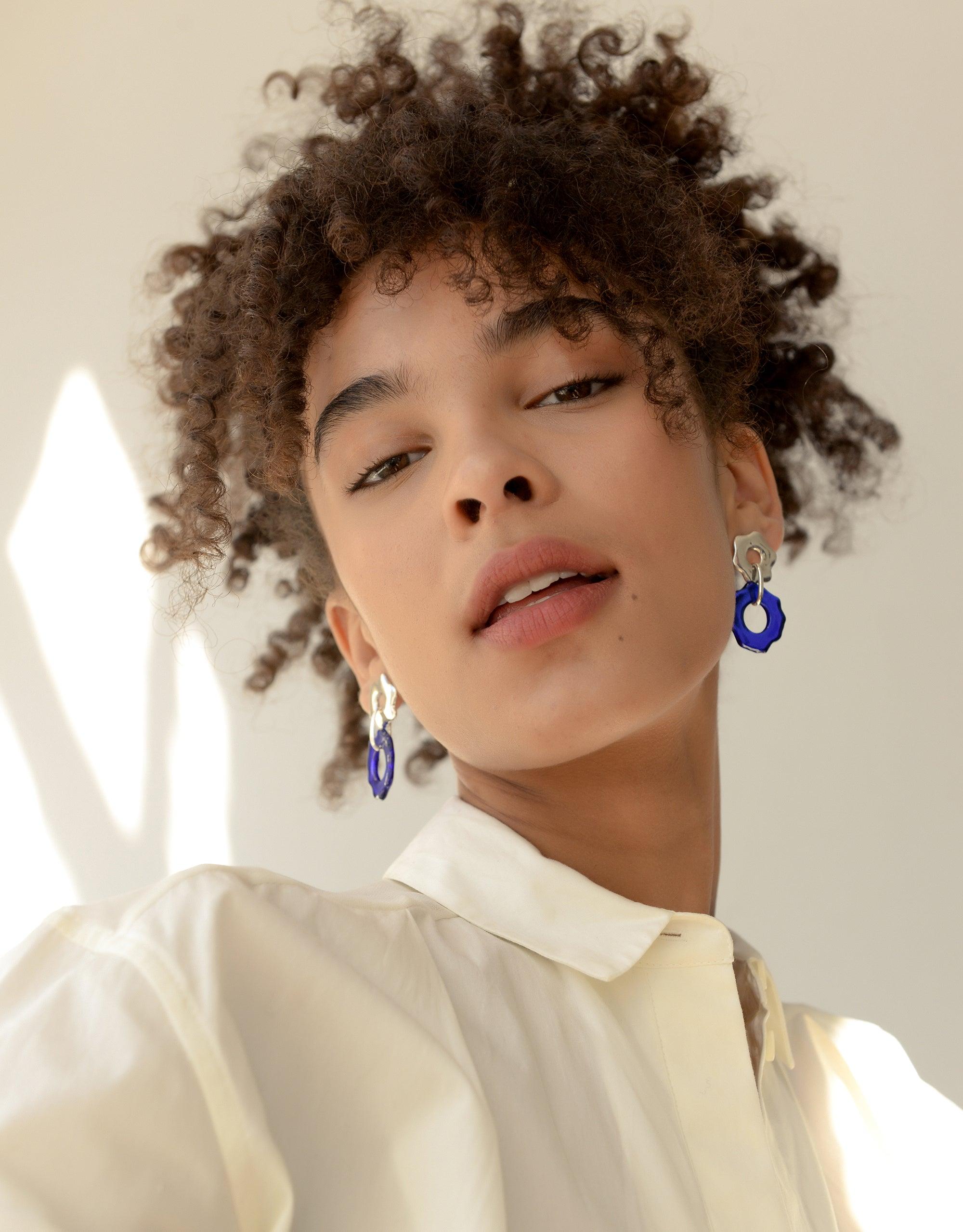 Elegant model wearing Avens Earrings, featuring blue eco-friendly glass accents. Handcrafted earrings inspired by Arctic mountain avens flower, showcasing sustainable jewelry design. Avens Earrings by CLED
