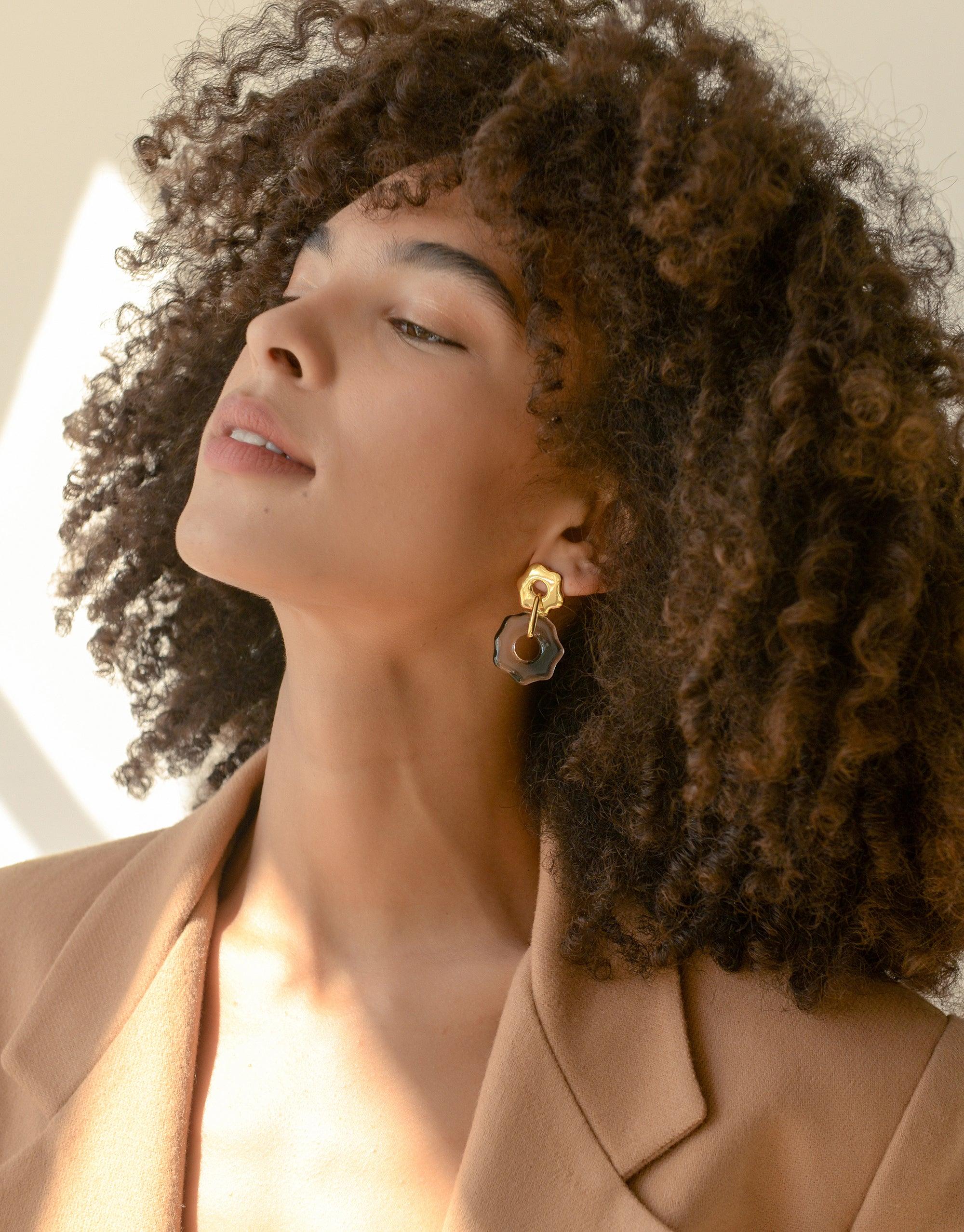 Profile view of a person with curly hair wearing Avens Earrings, showcasing handcrafted eco-friendly jewelry with unique glass design. Sustainable fashion accessory for climate awareness. Avens Earrings by CLED.