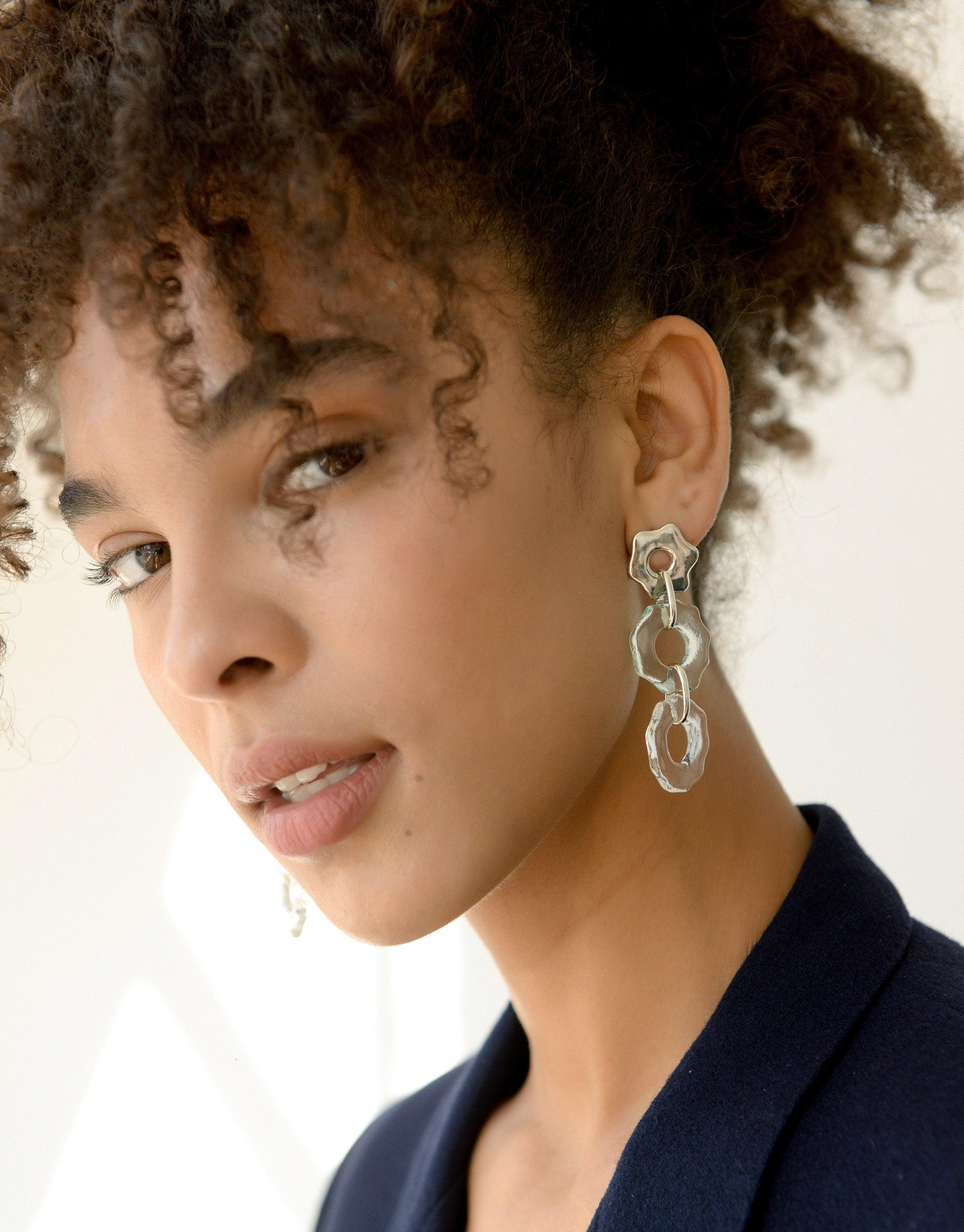 Close-up of Avens Earrings Trio, featuring three connected organic shapes in silver, worn by a model with curly hair. The earrings showcase a distinctive floral-inspired design, emphasizing their eco-friendly and handcrafted nature. Avens Earrings Trio by CLED.