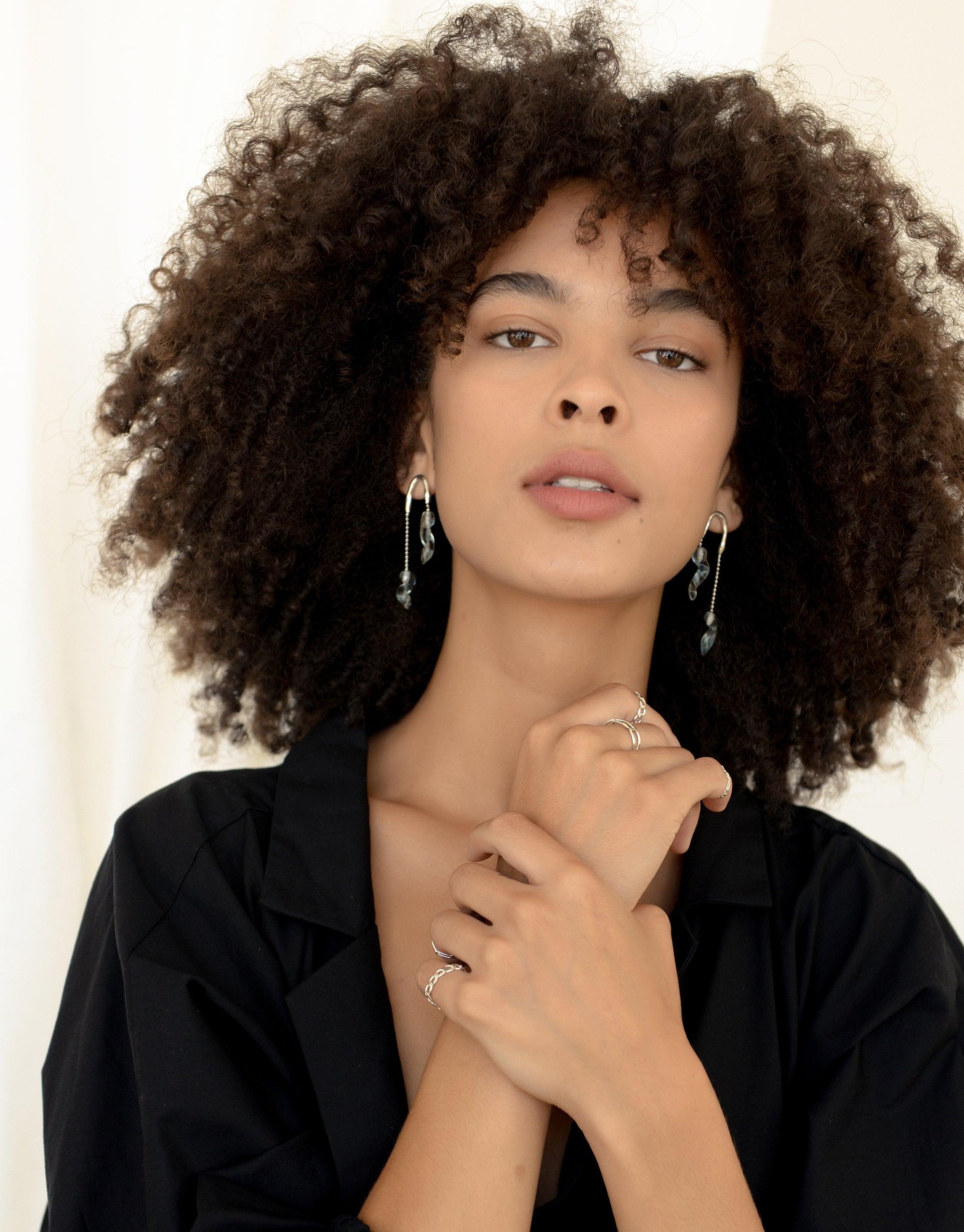 Elegant model wearing Crystal Drops Earrings from the Floating Glacier Collection, showcasing asymmetrical design inspired by icicles. Delicate eco-friendly jewelry in sky blue ice color, handcrafted from repurposed glass. Sustainable fashion accessory by CLED.