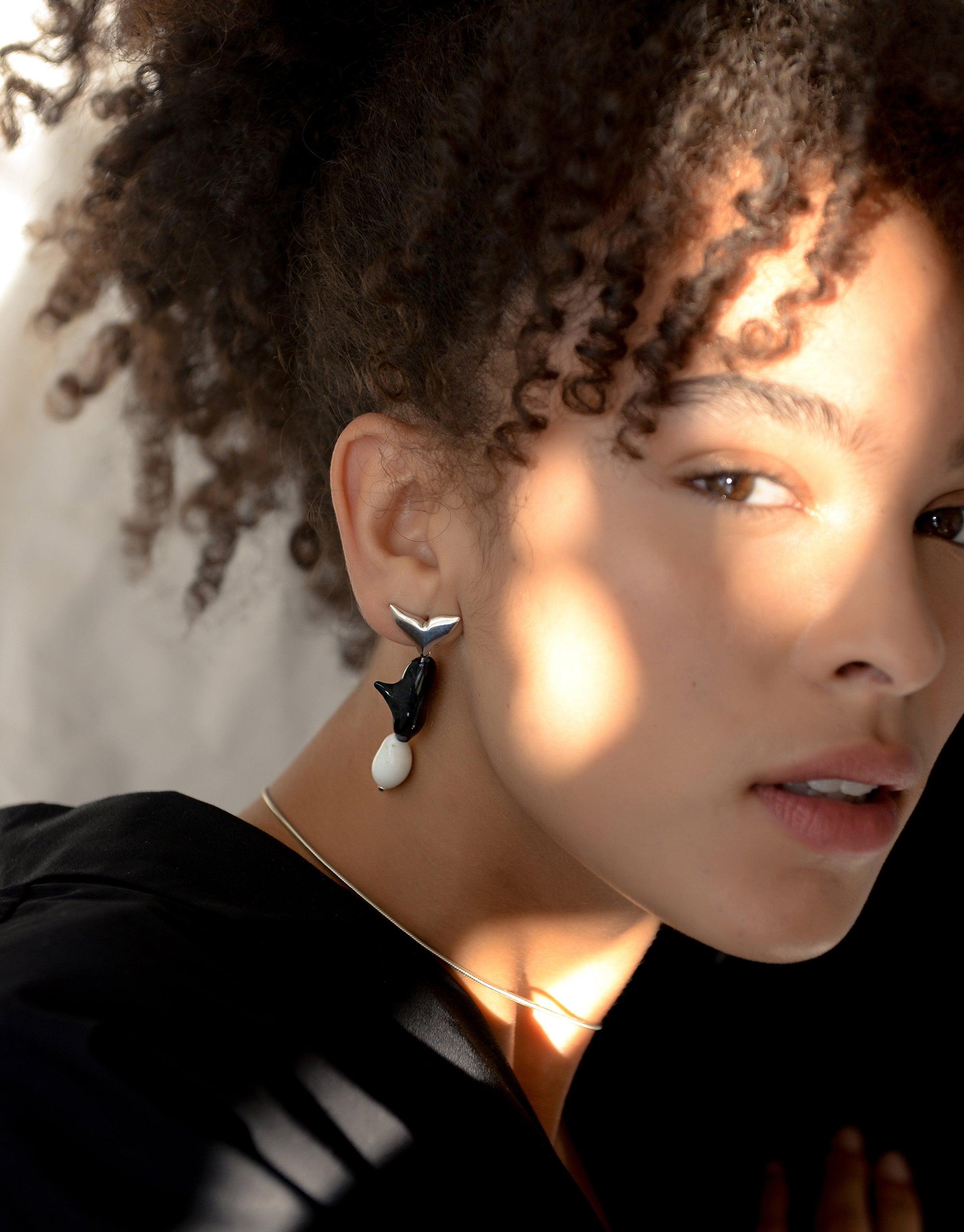 Close-up of model wearing Orca Earrings, featuring black and white design with eco-friendly glass bead. Part of the Floating Glacier Collection, highlighting climate change awareness. Handcrafted sustainable jewelry by CLED.